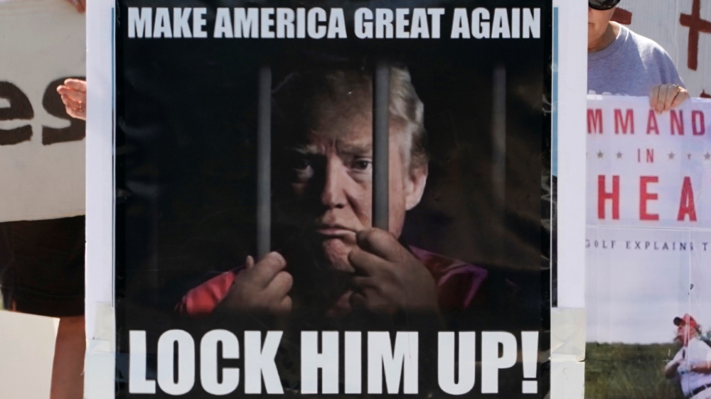 Protesters hold signs outside Trump National Golf Club in Sterling