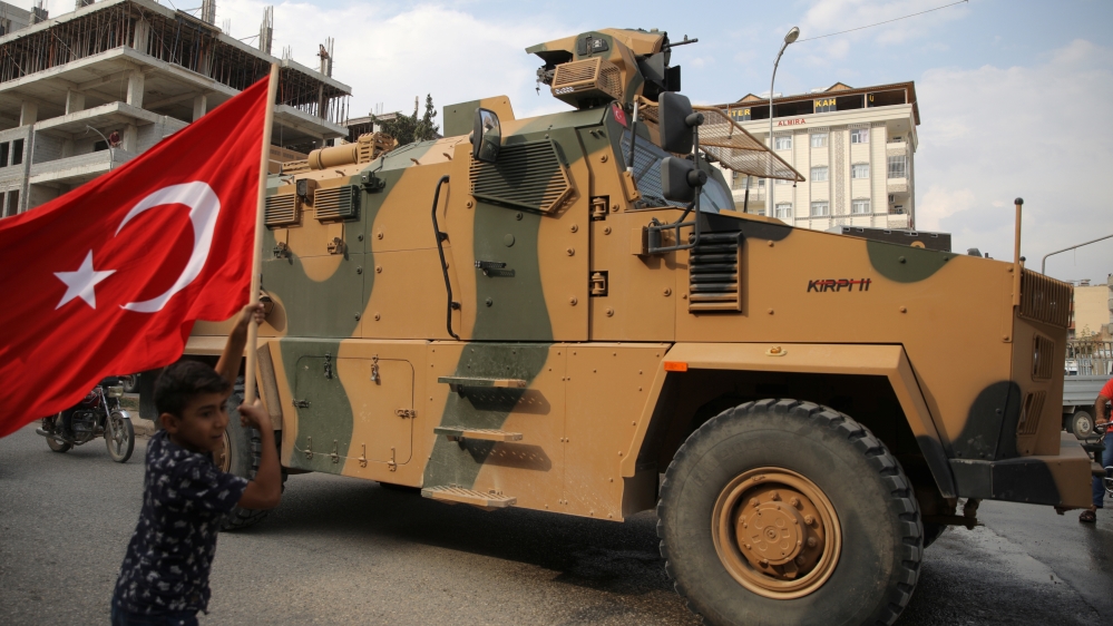 Boy waves a Turkish flag as Turkish military vehicles drive on a street in the Turkish border town of Akcakale