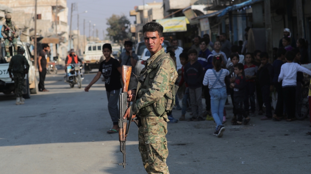 A Turkey-backed Syrian rebel fighter holds a weapon as he stands along a street in the border town of Tal Abyad
