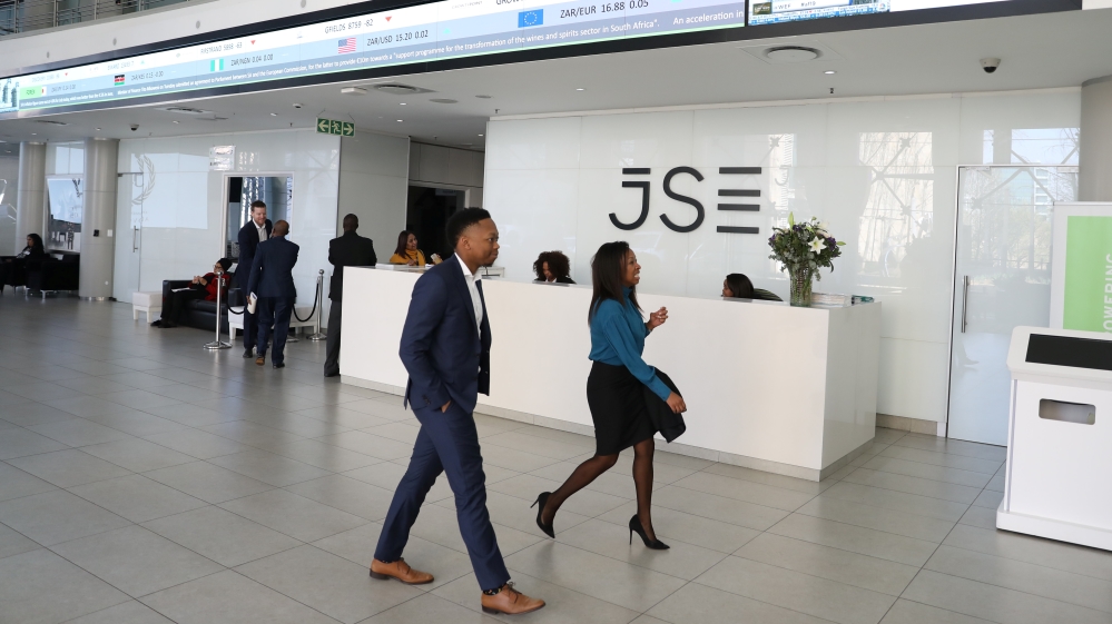 Visitors walk past a reception with an electronic board displaying movements in major indices at the Johannesburg Stock Exchange building in Sandton, Johannesburg