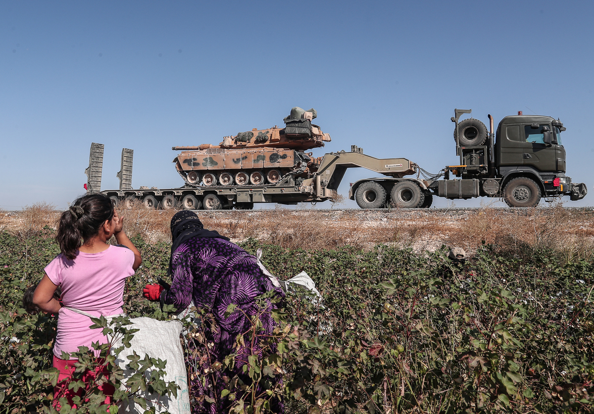 Seasonal workers cut a cotton while Turkish military vehicles carrying tanks as they are on the way to Northern Syria for a military operation in Kurdish areas, near the Syrian border, near Akcakale d
