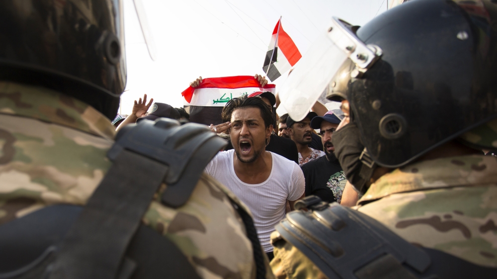 An Iraqi protestor gestures in front of security forces