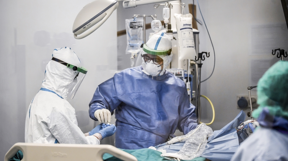 In this photograph taken from behind a window, doctors work on a Covid-19 patient in the intensive care unit of San Matteo Hospital, in Pavia, northern Italy, Thursday, March 26, 2020. The San Matteo
