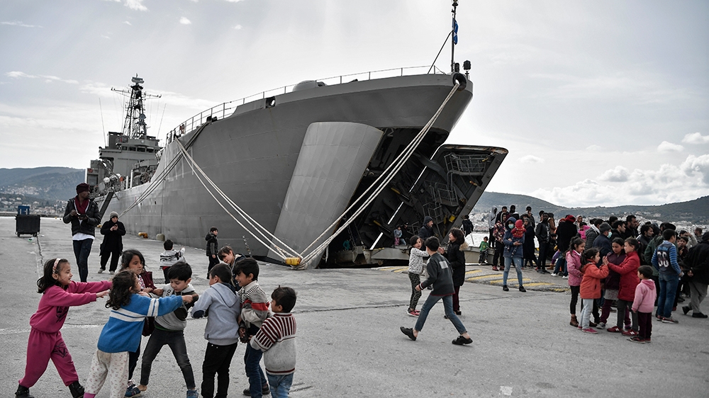 Children play past the military carrier which accomodates refugees and migrants arrived on Lesbos island after March 1, in the port of Mytilene on the island of Lesbos on March 7, 2020. (Photo by LOUI