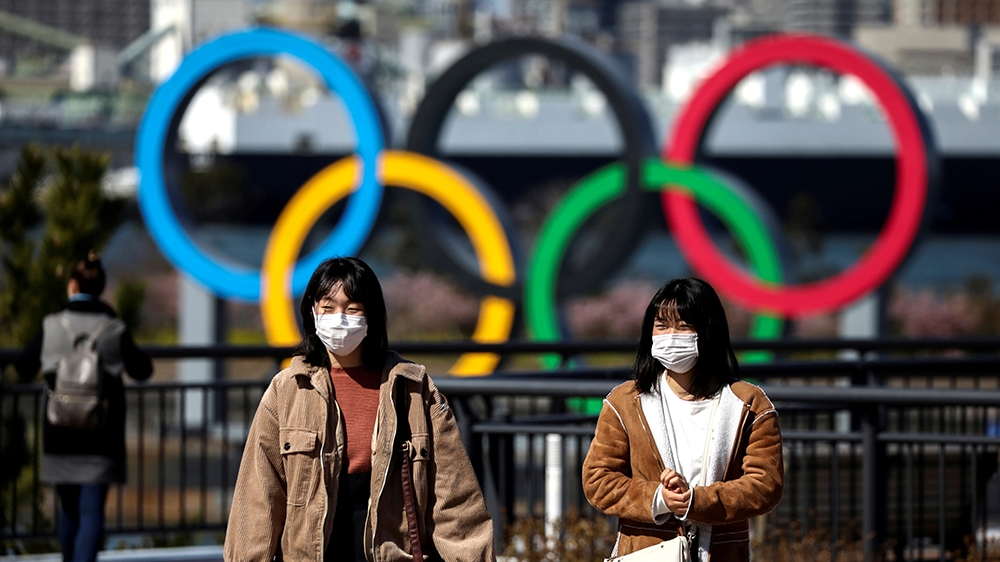FILE PHOTO: People wearing protective face masks, following an outbreak of the coronavirus, are seen in front of the Giant Olympic rings at the waterfront area at Odaiba Marine Park in Tokyo, Japan, F