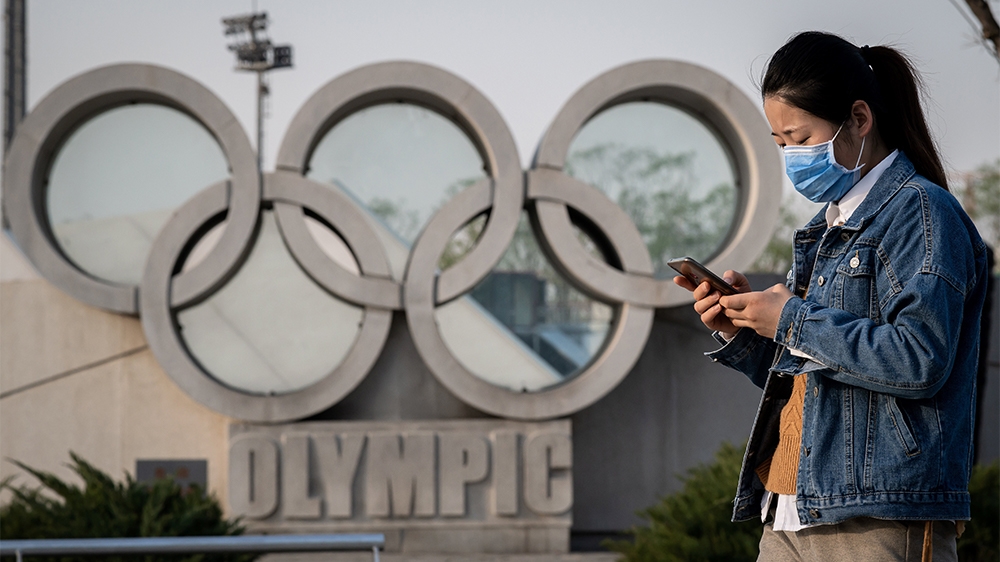 A woman wearing a face mask, amid concerns of the COVID-19 coronavirus, walks before an Olympic rings sculpture at the national ''Birds Nest'' stadium, the main site of the 2008 Beijing Olympics in Beij