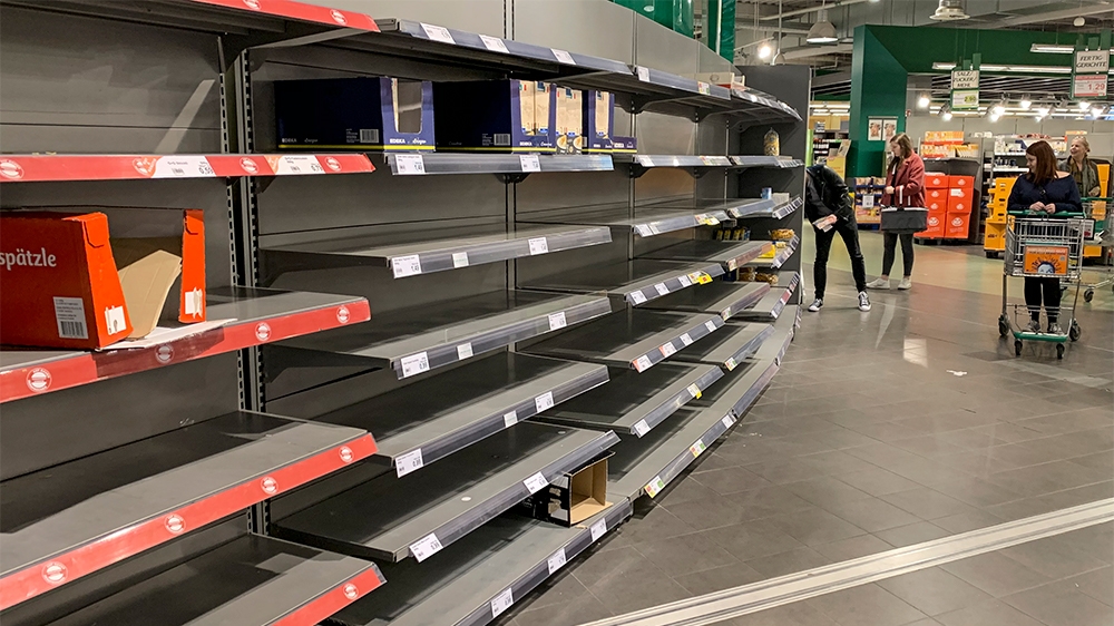Customers stand in front of empty grocery shelves in a big supermarket in Gelsenkirchen, Germany, Monday, March 16, 2020. Some food stores see an unprecedented stockpiling brought on by the coronaviru