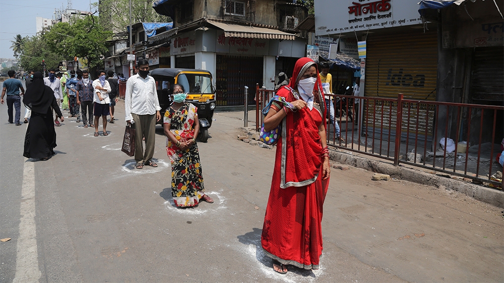 Indians stand in marked positions to buy essential commodities from a grocery store in Mumbai, India, Wednesday, March 25, 2020.The world's largest democracy went under the world's biggest lockdown We