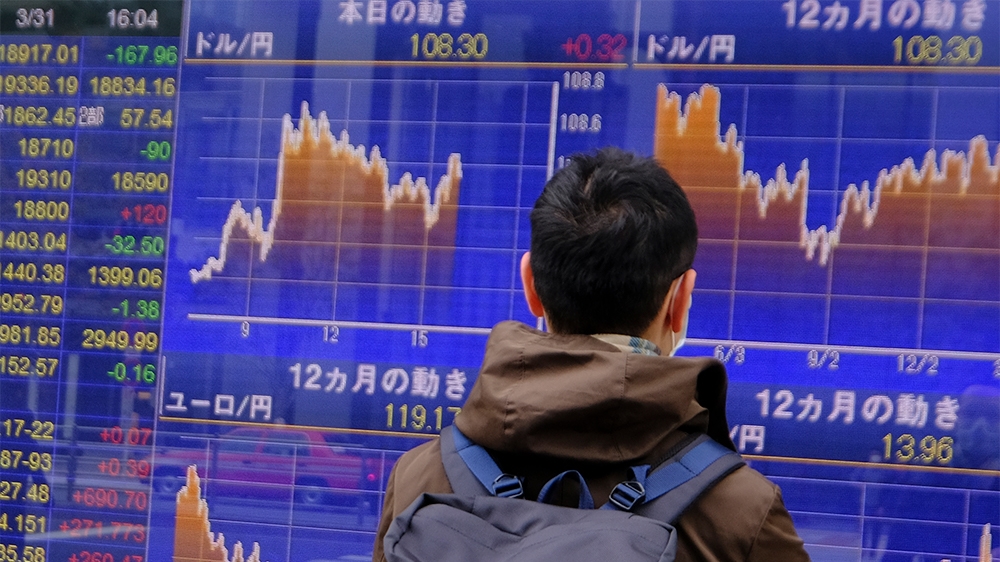 A man looks at movements of the foreign exchange rate against the US dollar (upper) in Tokyo on March 31, 2020. - Tokyo shares closed lower on March 31 in volatile trade, as investors remained nervous