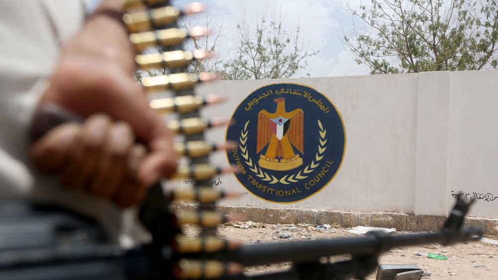 A Yemeni government soldier holds a weapon as he stands by an emblem of the STC at the headquarters of the separatist Southern Transitional Council in Ataq