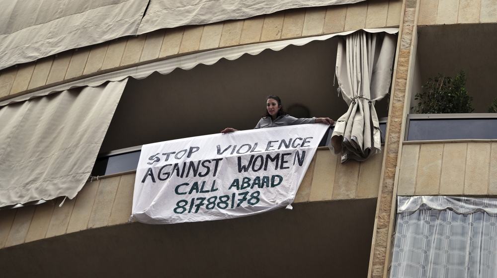 A woman hangs a banner from her balcony with the number of a domestic violence hotline during a national lockdown aimed at stemming the spread of coronavirus, in Beirut, Lebanon, Thursday, April 16, 2