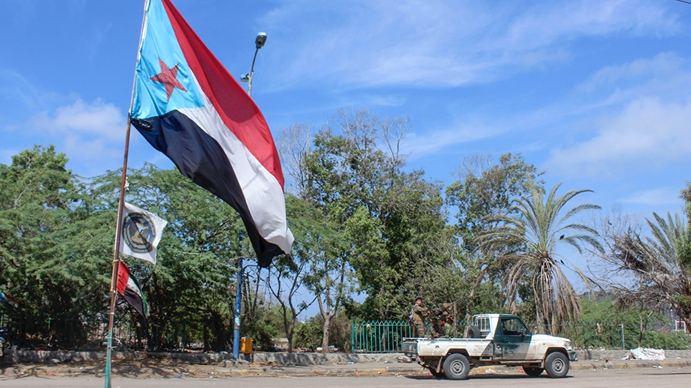 Fighters drive a vehicle past a separatist flag (the old flag of South Yemen).