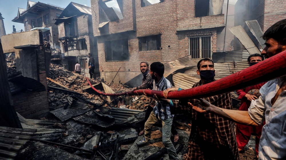 People hold a hosepipe amidst the smoldering debris of residential houses that, according to local media reports, were damaged during a gun battle between Indian security forces and suspected militant