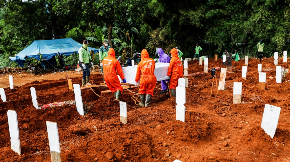 Workers wearing protective suits prepare to bury a coffin at the Muslim burial area provided by the government for victims of the coronavirus disease (COVID-19) at Pondok Ranggon cemetery complex in J