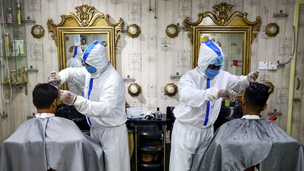 Barbers wearing protective suits provide hair cut service to the customers, in Dhaka
