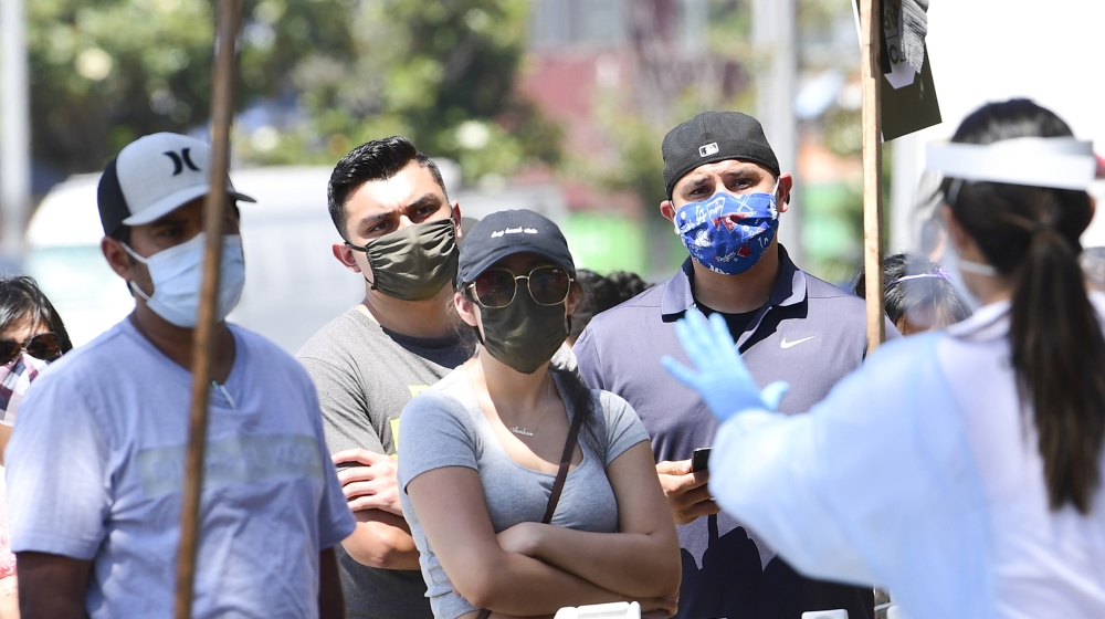 A COVID-19 test site volunteer wearing personal protective equipment gives directions to people waiting in line at a walk-in coronavirus test site in Los Angeles, California on July 10, 2020 as the st