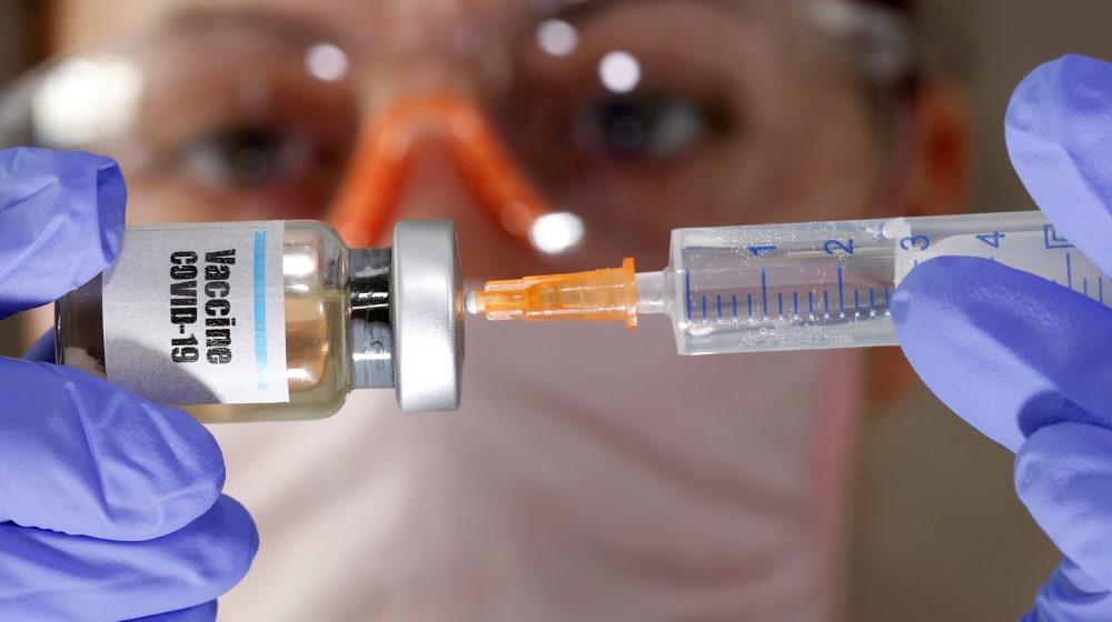 A woman holds a small bottle labeled with a "Vaccine COVID-19" sticker and a medical syringe in this illustration taken April 10, 2020. REUTERS/Dado Ruvic/Illustration/File Photo