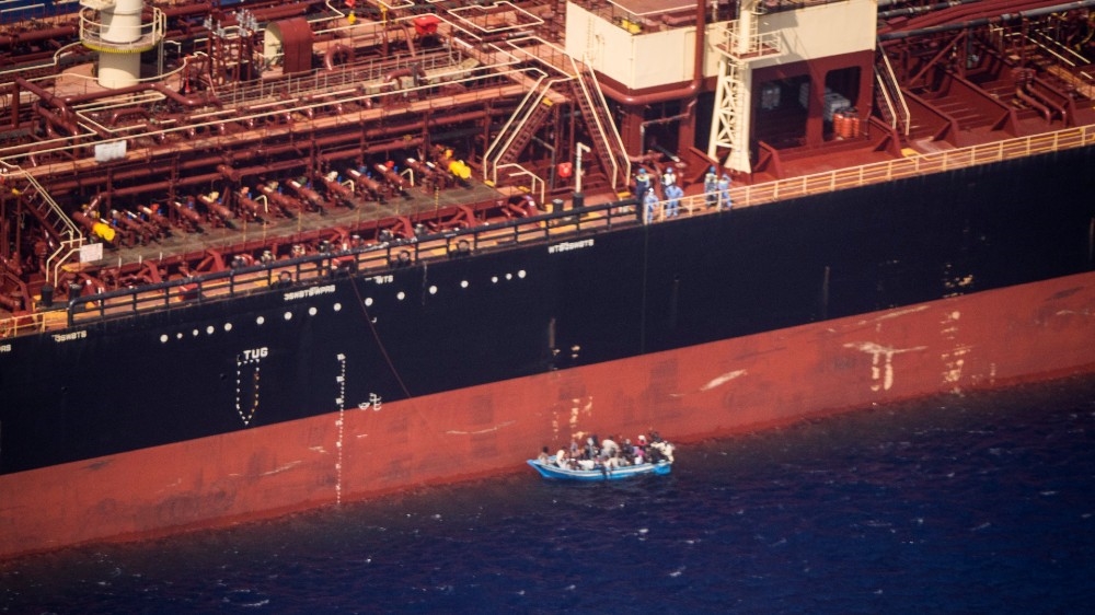 Migrants sit in a boat alongside the Maersk Etienne tanker