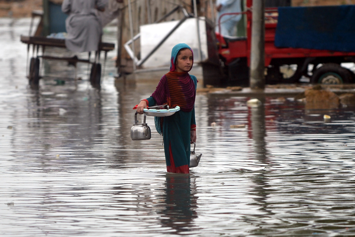 A girl carries a tea kettle as she wades through a flooded street after heavy monsoon rains in Pakistan''s port city of Karachi on August 25, 2020. (Photo by Rizwan TABASSUM / AFP)