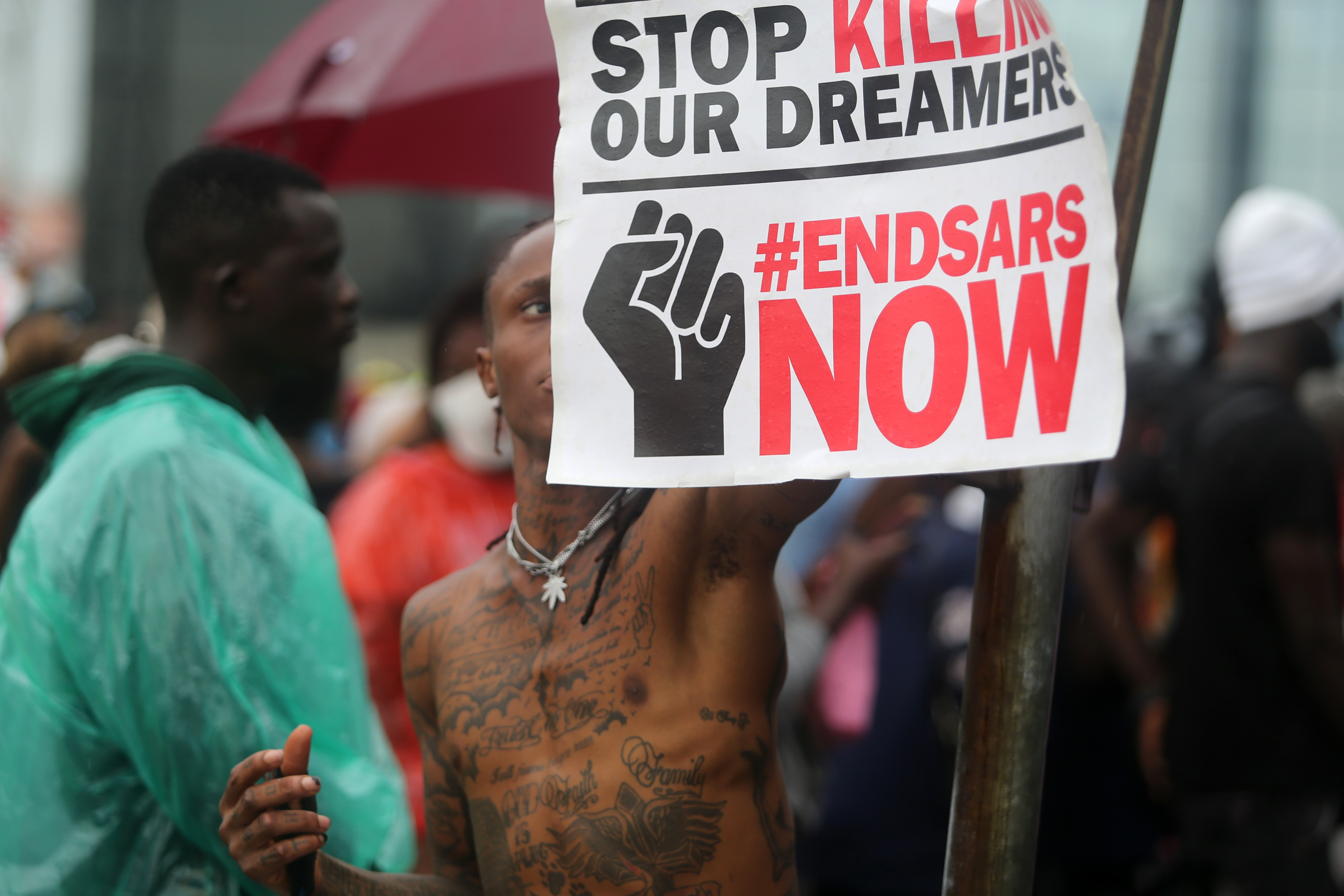 A protesters with a tattoo on his body holds a banner during a protest against the Nigeria rogue police, otherwise known as Special Anti-Robbery Squad (SARS), in Lekki district of Lagos [Akintunde Akinleye/EPA]