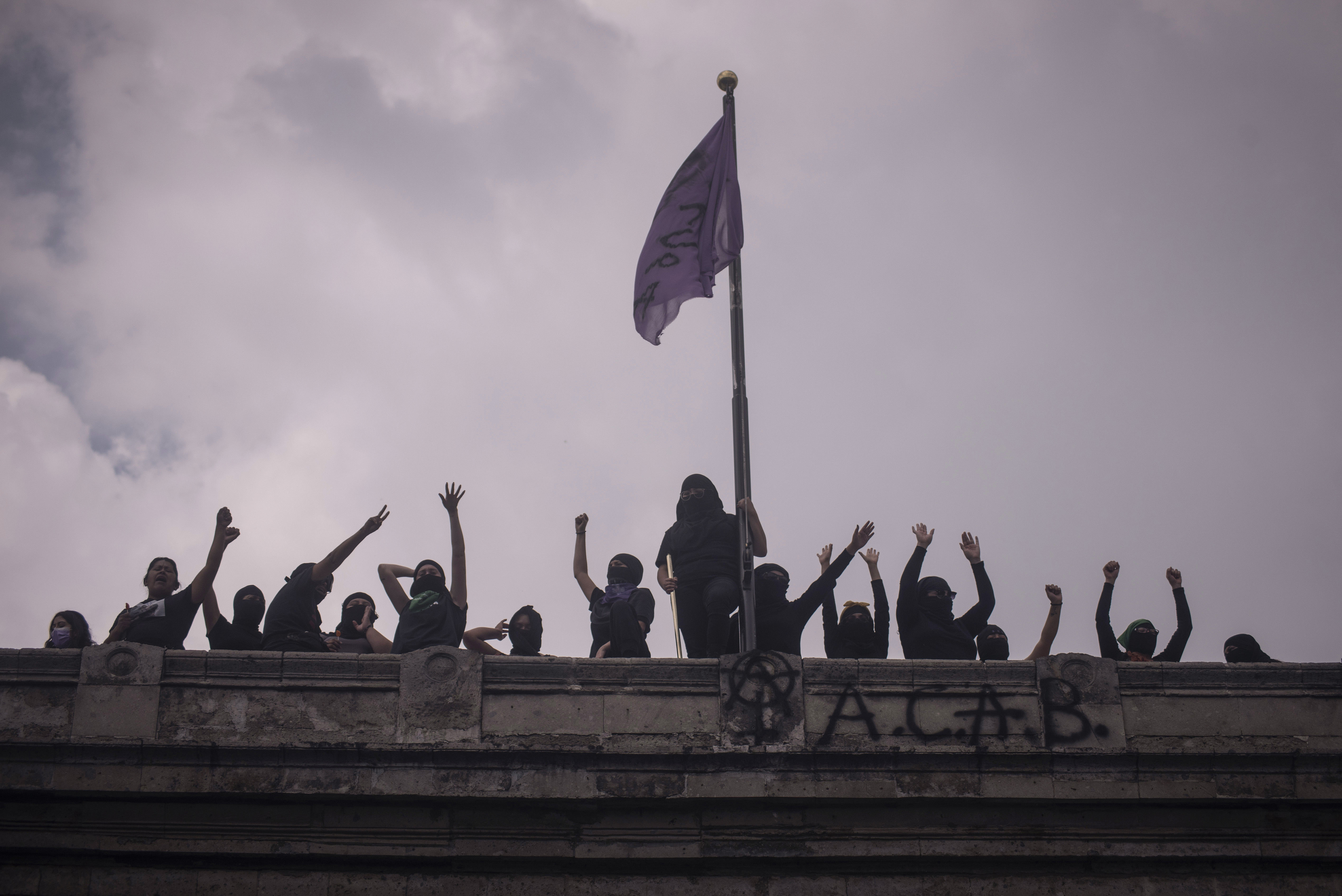 The feminist Black Block protesters shout from the rooftop of the National Human Rights Commission building, now the Okupa Cuba Casa Refugio, (Cuba Occupation-Shelter House) in Mexico City, Mexico, on September 16, 2020 [Victoria Razo/Al Jazeera]