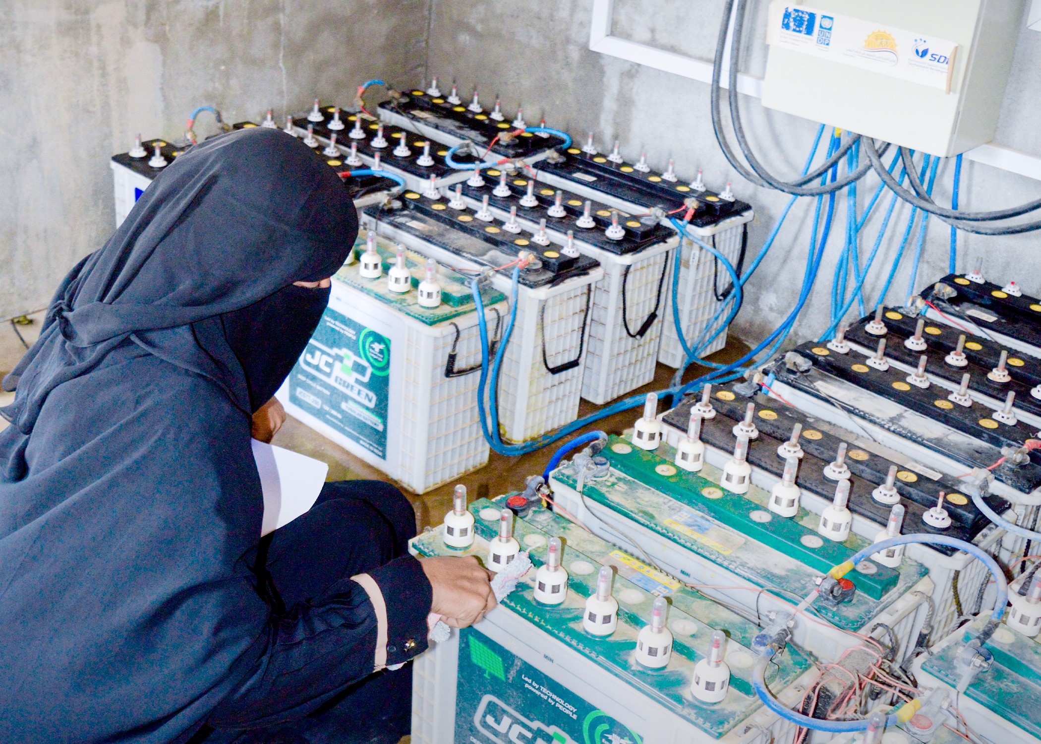 A woman checks batteries at the Abs solar microgrid station [Photo courtesy of SDF YEMEN]