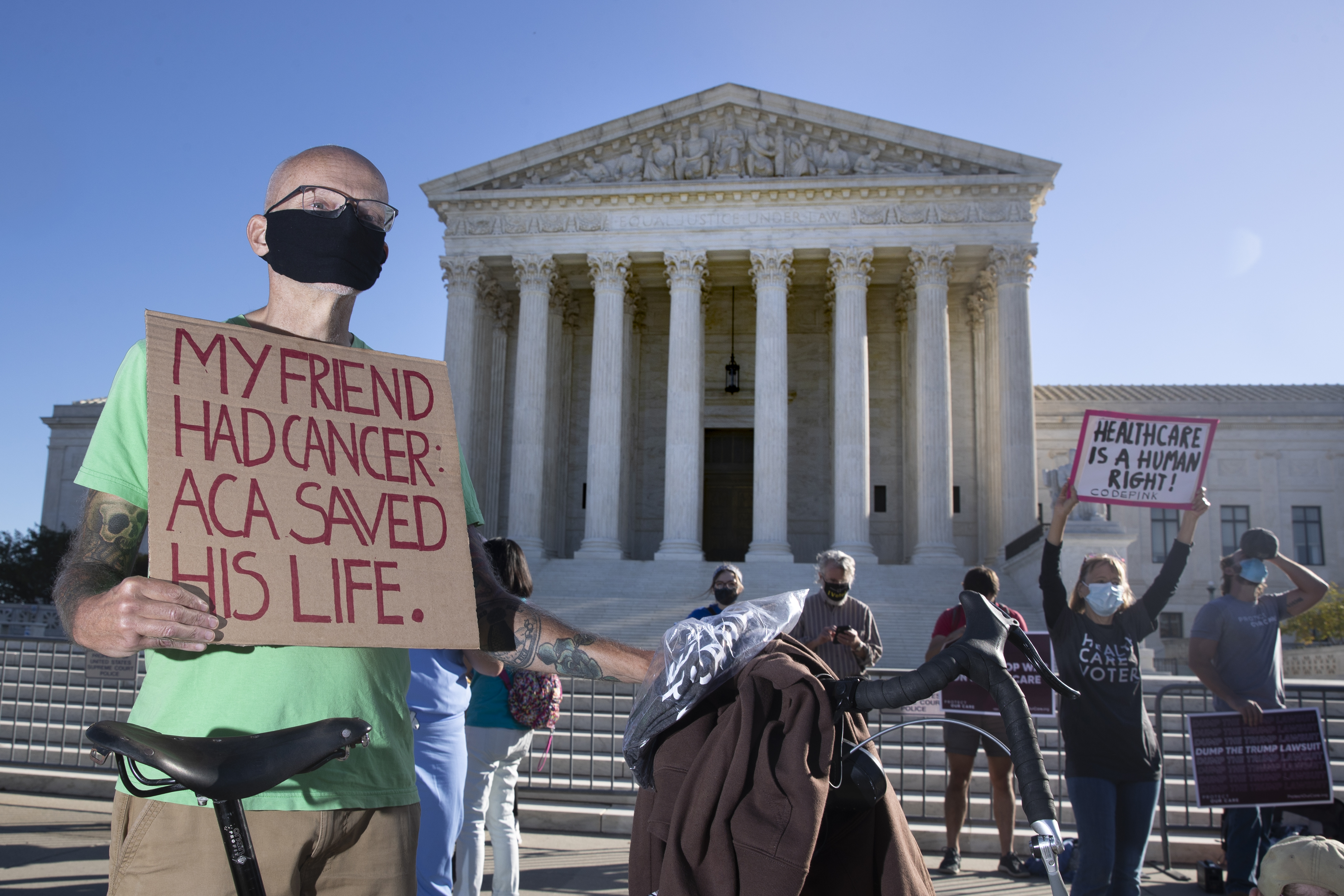 A person holds up a sign stating "My friend had cancer. ACA saved his life."
