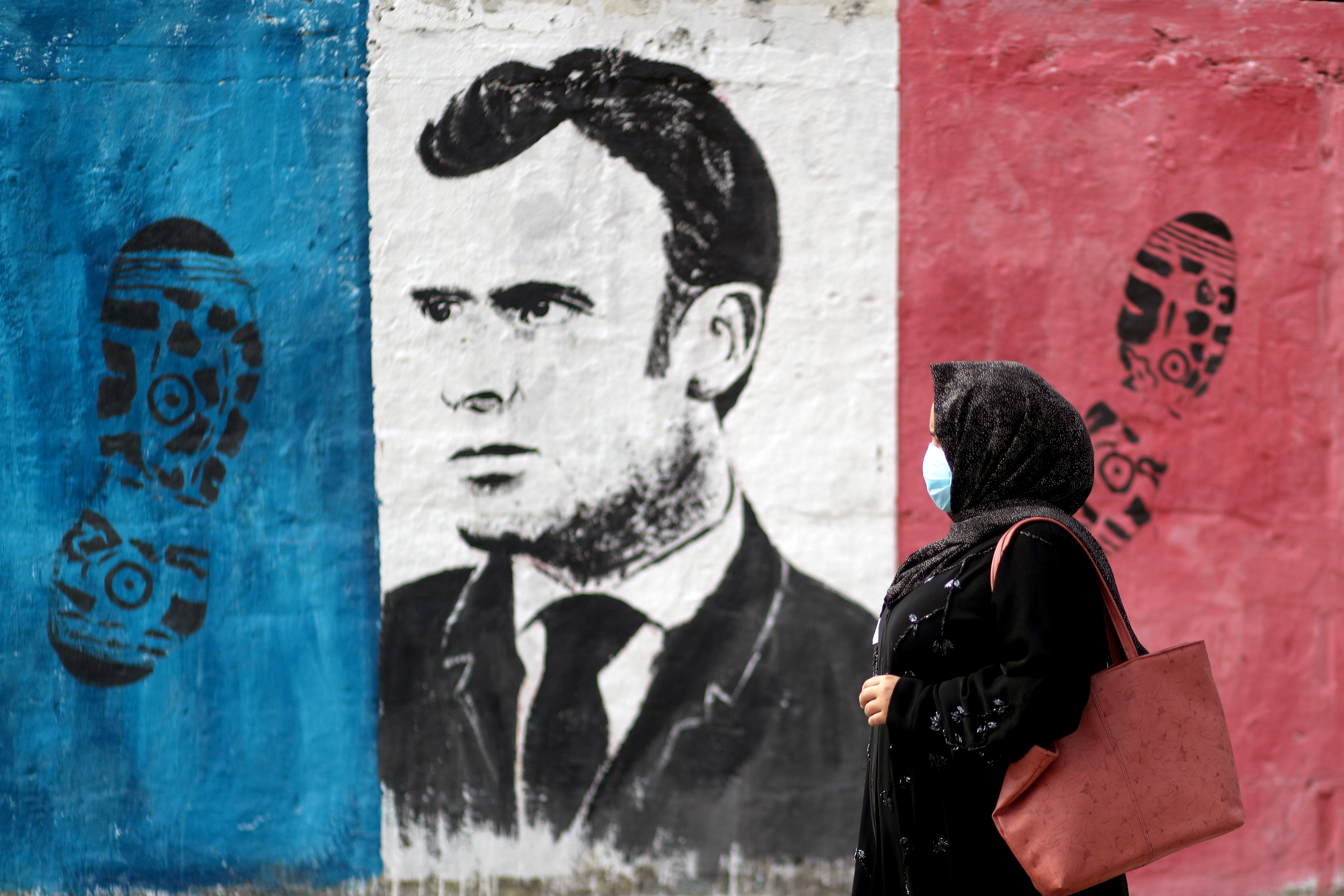 A Palestinian woman walks past an anti-French President Emmanuel Macron mural painted by an artist to protest against the publications of a cartoon of Prophet Mohammad in France and Macron's comments, in Gaza City, October 28, 2020. [Mohammed Salem/Reuters]