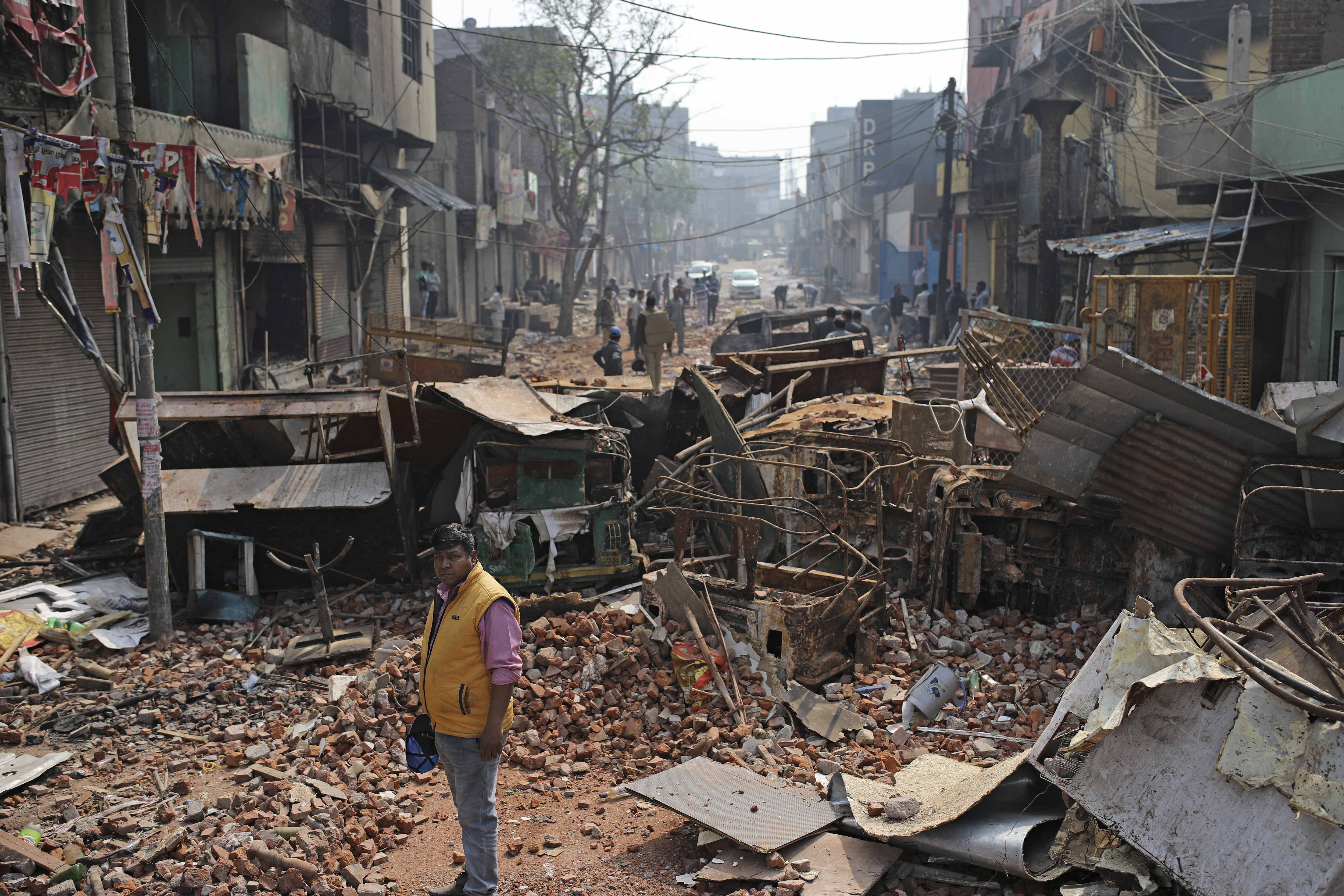A Delhi municipal worker stands next to the remains of vehicles, steel cupboards and other materials on a street vandalised during the violence in New Delhi, India on February 27, 2020 [File: AP/Altaf Qadri]