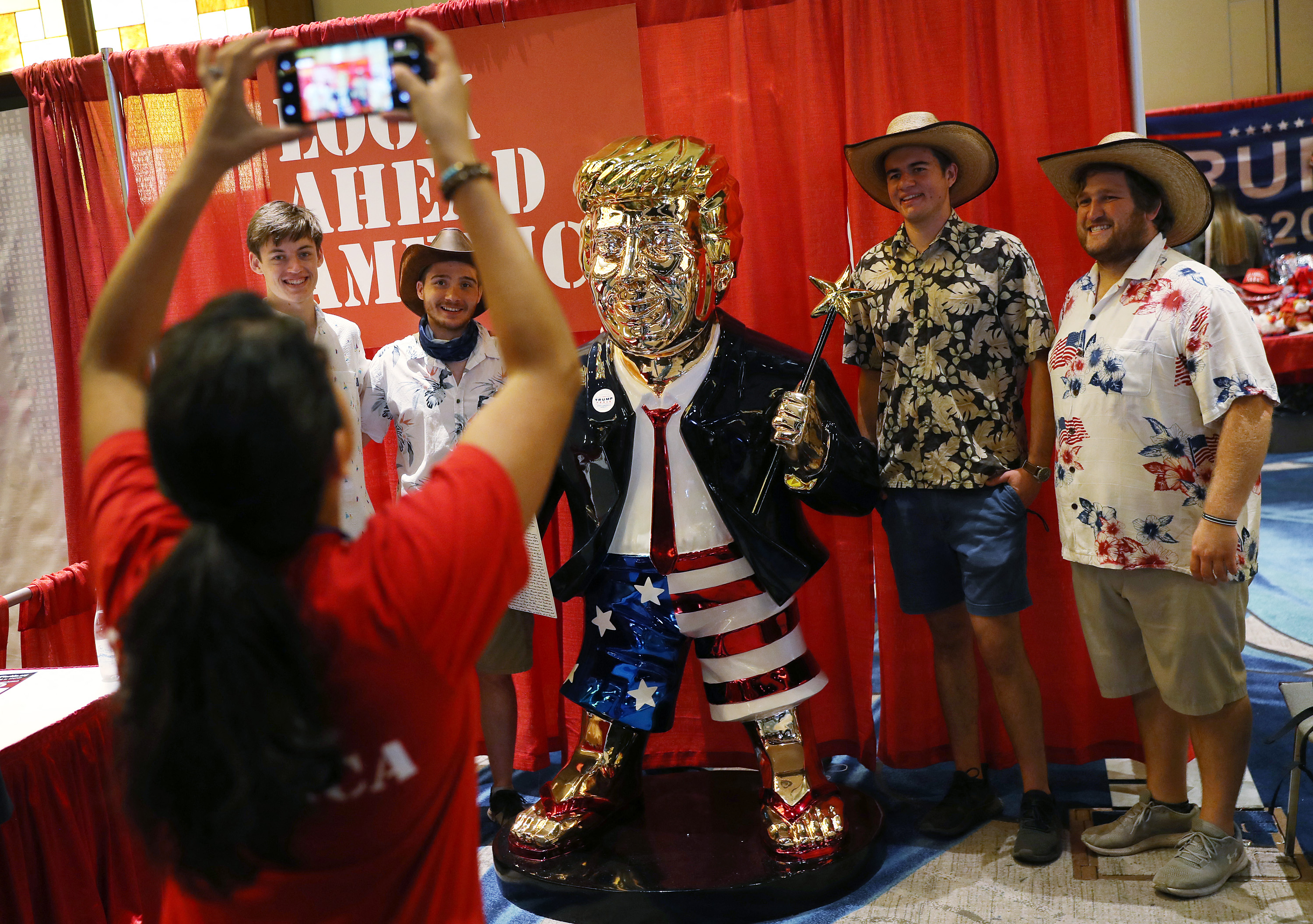 People take a picture with a gold statue of former US President Donald Trump's statue on display at the Conservative Political Action Conference [Joe Raedle/Getty Images/AFP]