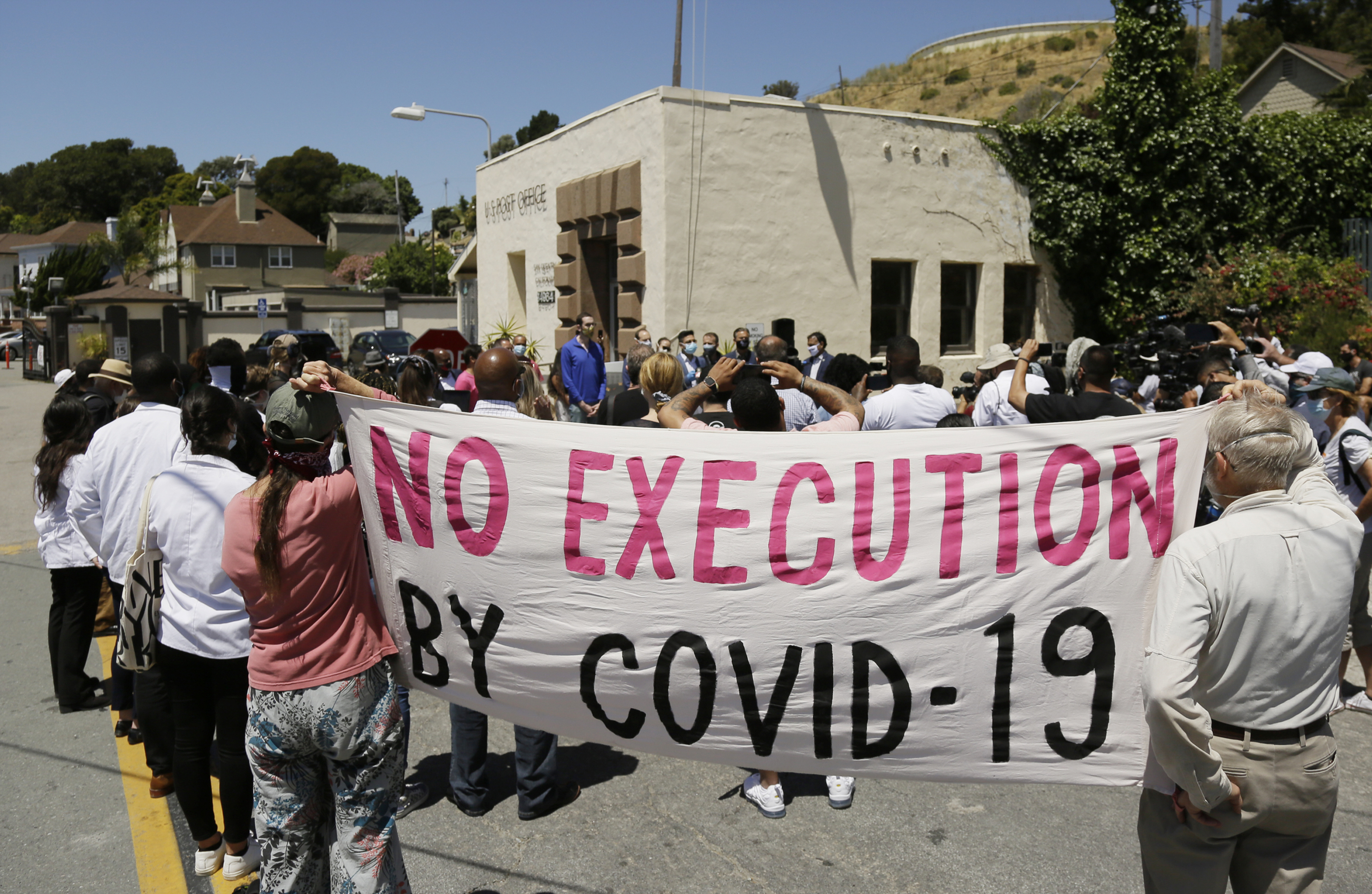 People hold up a banner while listening to a news conference outside San Quentin State Prison in California after a coronavirus outbreak in the facility in July 2020 [File: Eric Risberg/AP Photo]