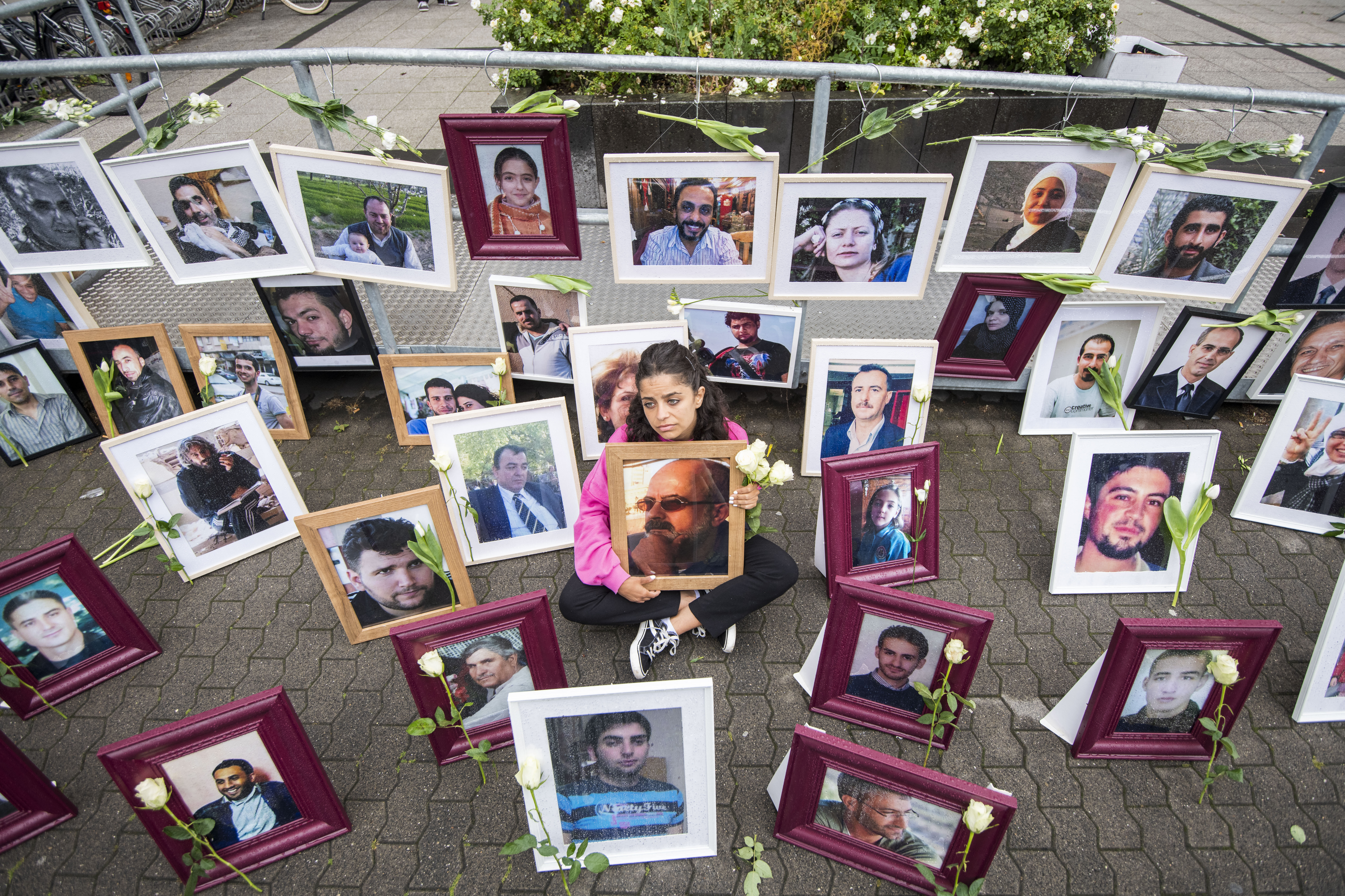 Syrian campaigner Wafa Mustafa sits between pictures of victims of the Syrian regime as she holds a picture of her father, during a protest outside the trial against two alleged Syrian former intelligence officers accused of crimes against humanity, in the first trial of its kind to emerge from the Syrian conflict, on June 4, 2020, in Koblenz, western Germany [File: Thomas Lohnes/AFP]
