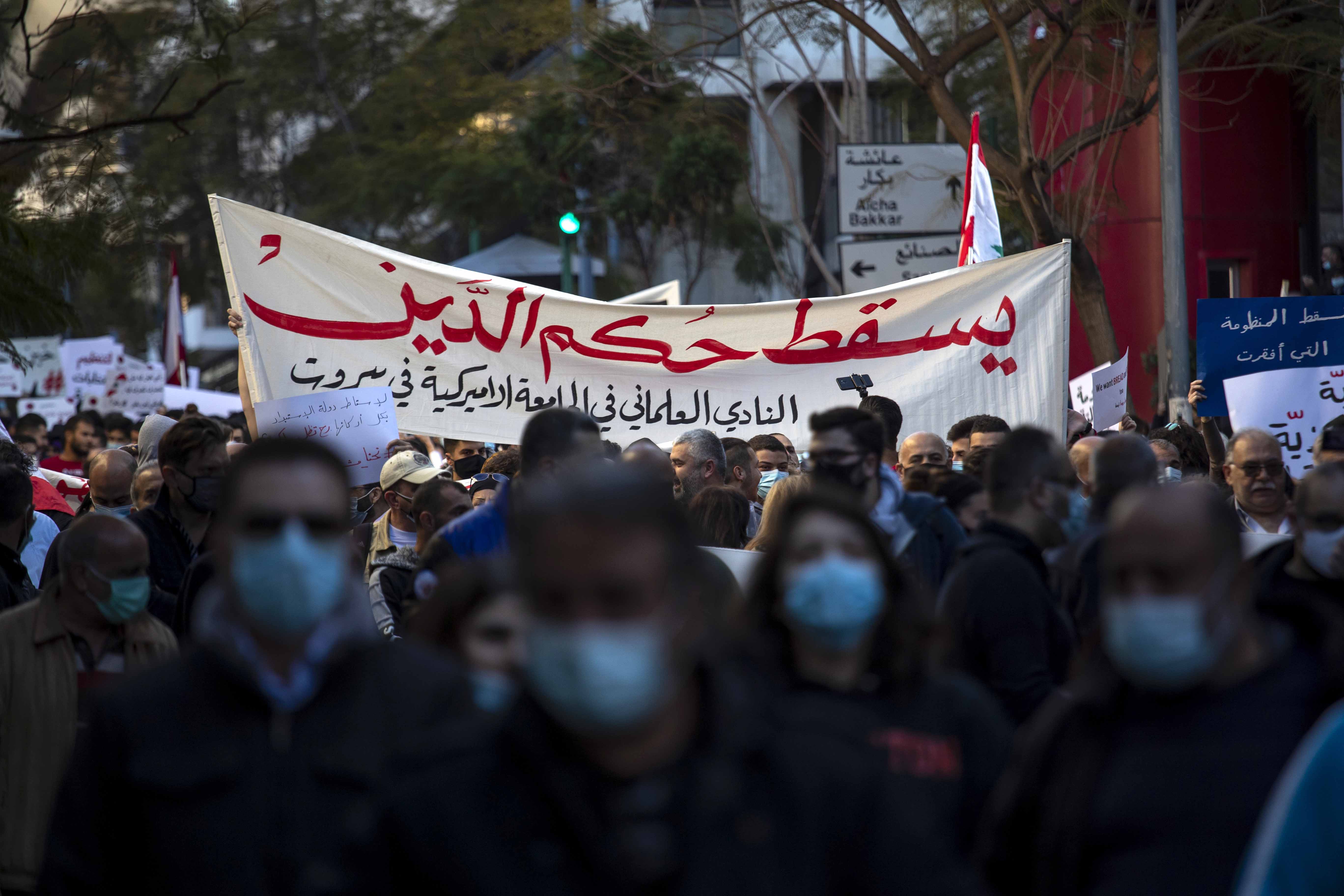 Anti-government protesters hold up a sign which reads 'Down with the rule of debt' during a protest against the rising prices and worsening economic conditions in Beirut, Lebanon on March 12, 2021 [AP/Hassan Ammar]