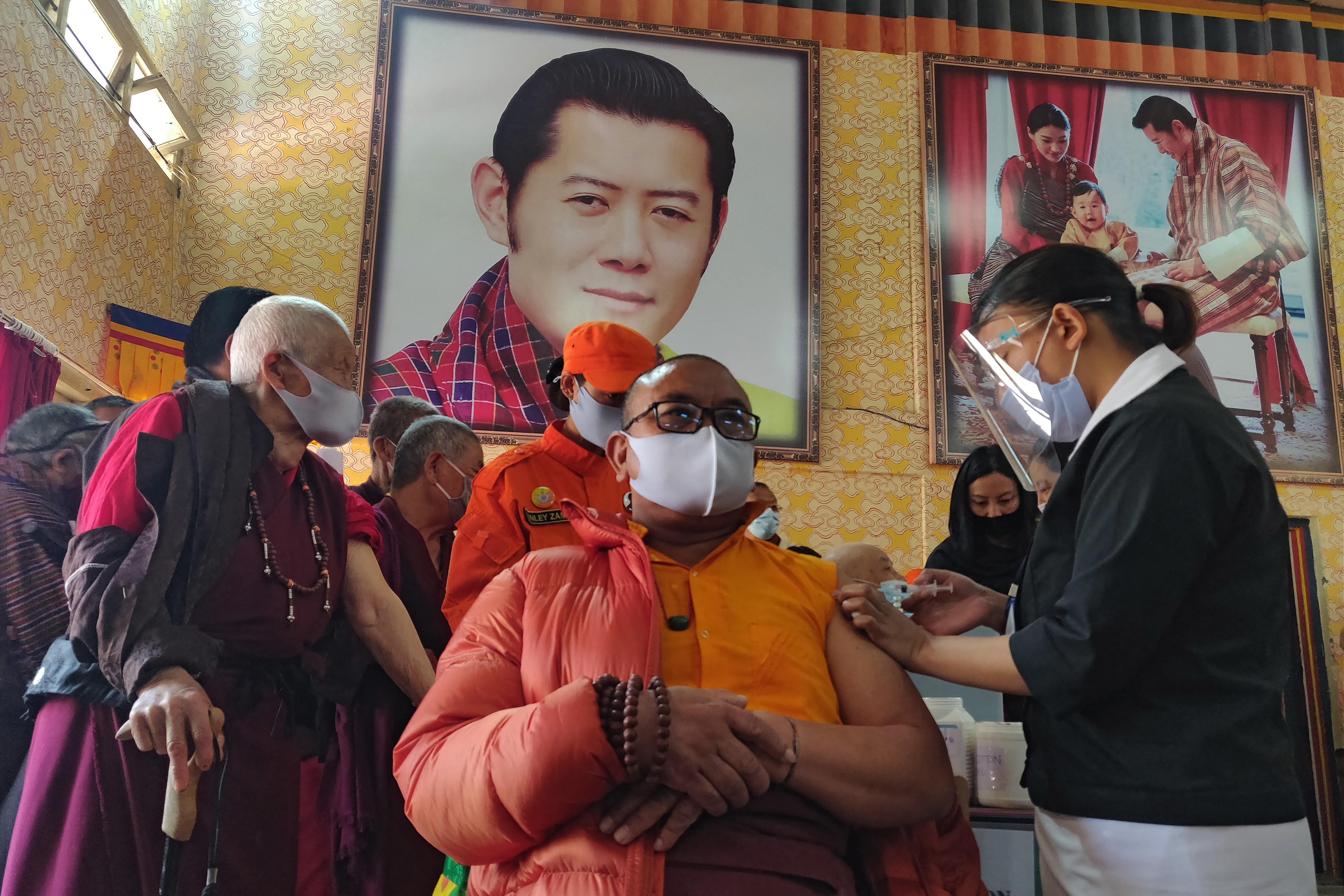 A health worker inoculates a Buddhist monk sitting in front of a portrait of Bhutan's King Jigme Khesar Namgyel Wangchuck, at Lungtenzampa Middle Secondary school in Thimphu [File: Upasana Dahal/AFP]