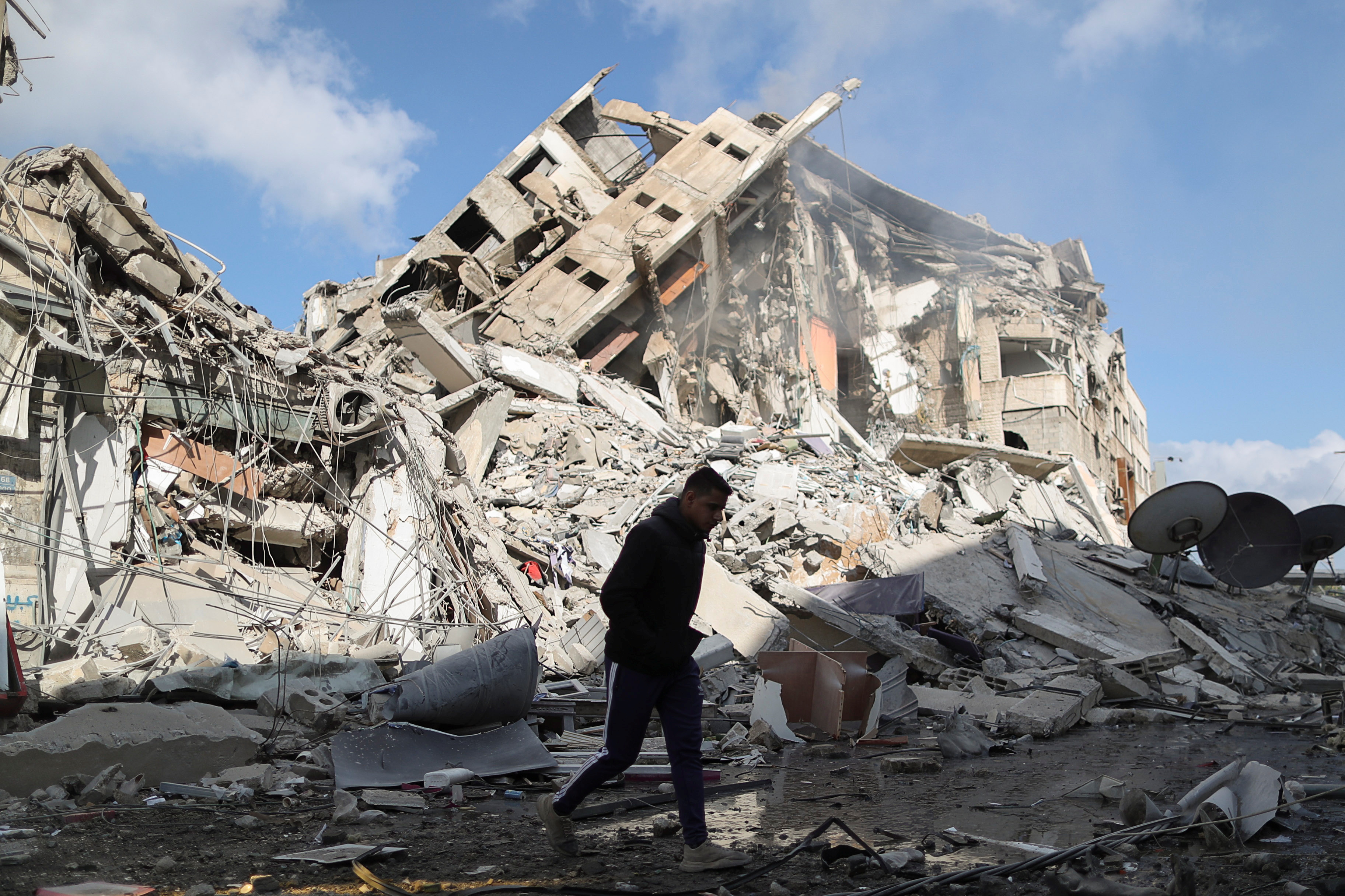 A Palestinian man walks past the remains of a tower which was destroyed by Israeli air strikes in Gaza City [Suhaib Salem/Reuters]