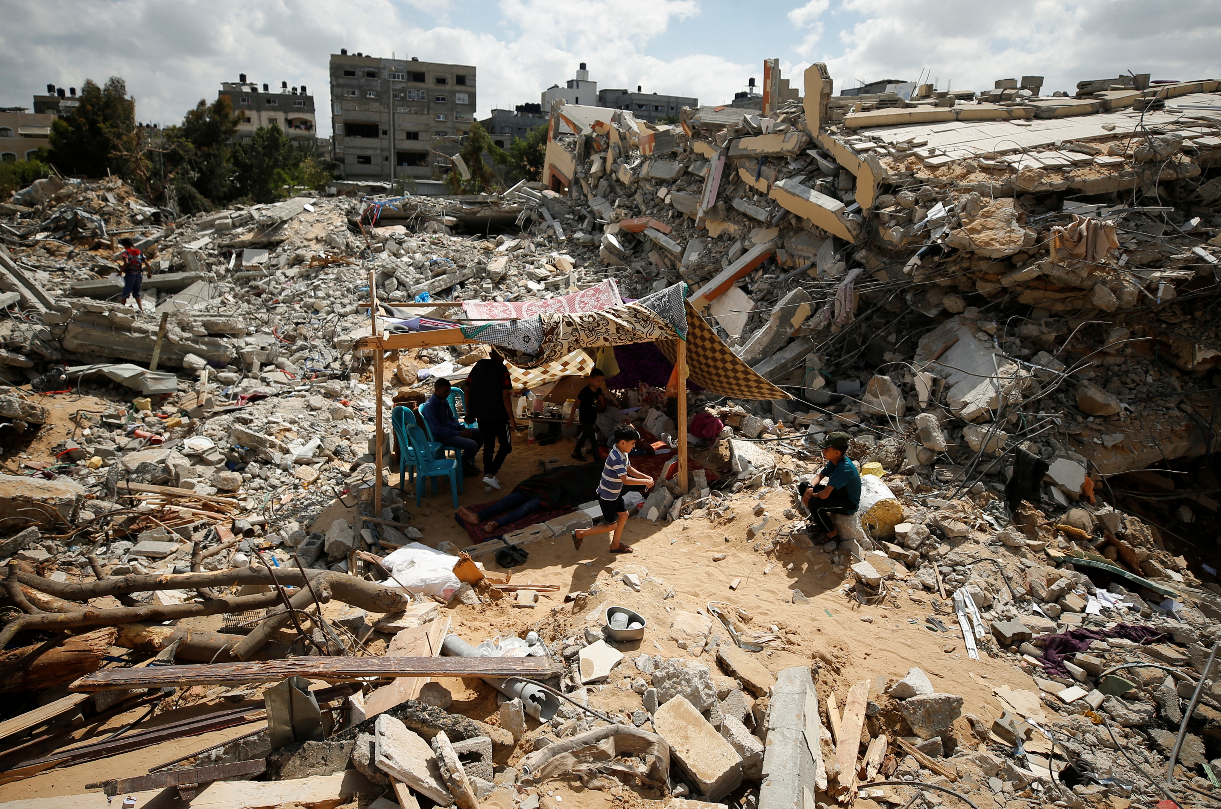 Palestinians sit in a makeshift tent in the rubble of their homes destroyed by Israeli air raids in Gaza [Mohammed Salem/Reuters]