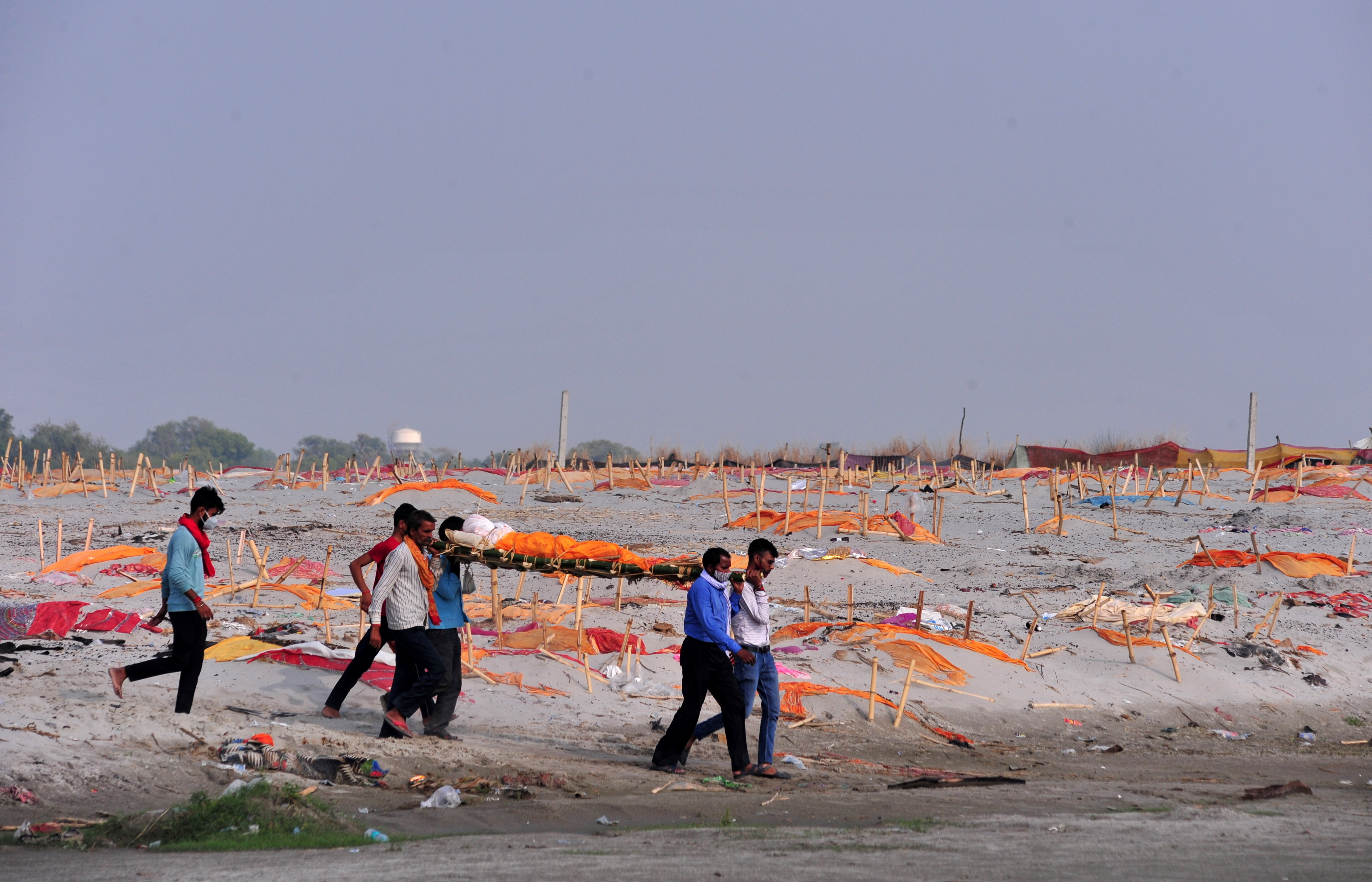 Relatives carry the body of a man for cremation after they, according to the relatives, were denied permission for his burial, past shallow sand graves of people, some of whom are suspected to have died from COVID-19, on the banks of the Ganges River in Shringverpur on the outskirts of Prayagraj, Uttar Pradesh [File: Ritesh Shukla/Reuters]