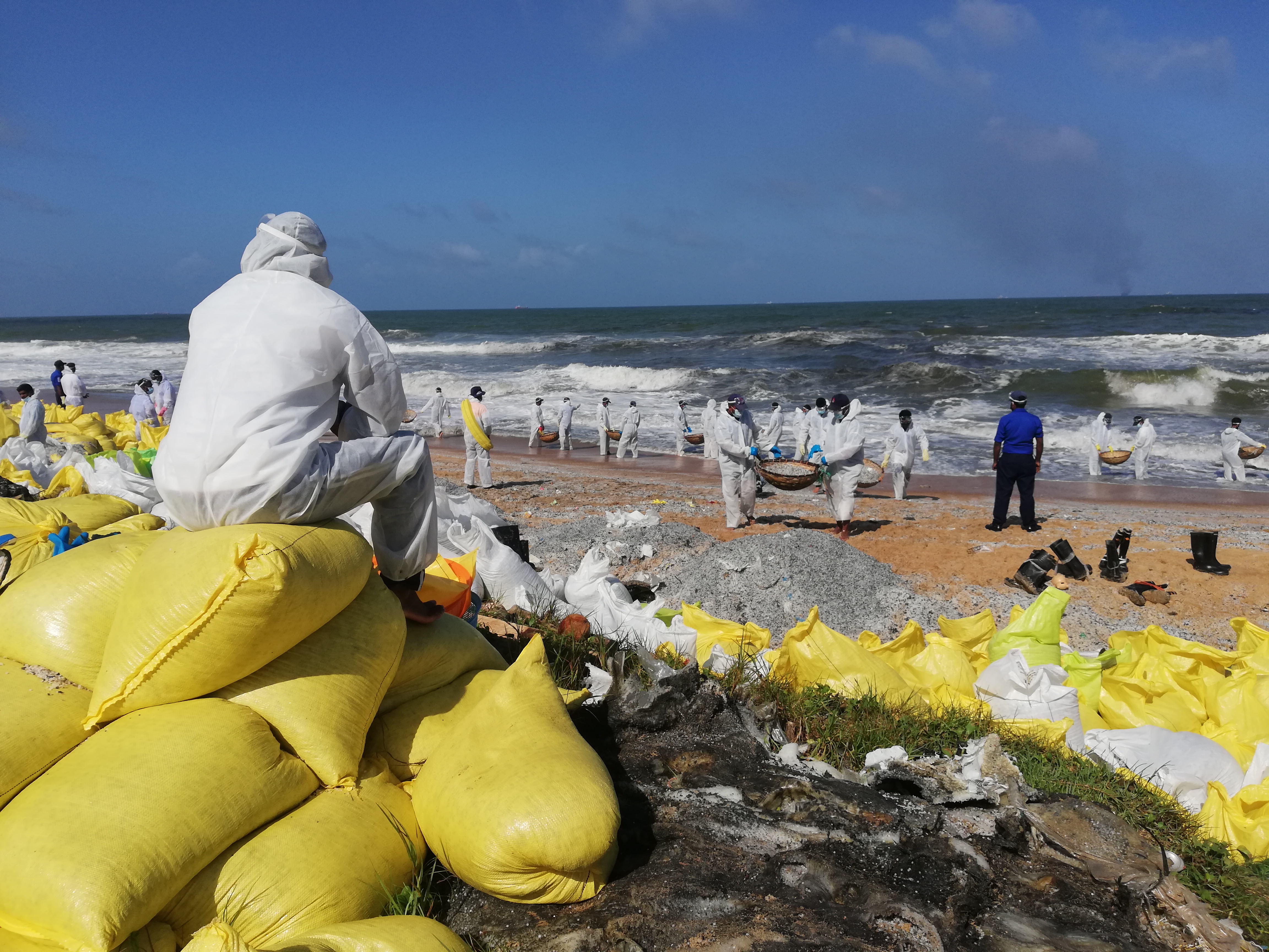 A Sri Lanka navy officer watches his colleagues collecting plastic pellets in Pamunugama [Aanya Wipulasena/Al Jazeera]