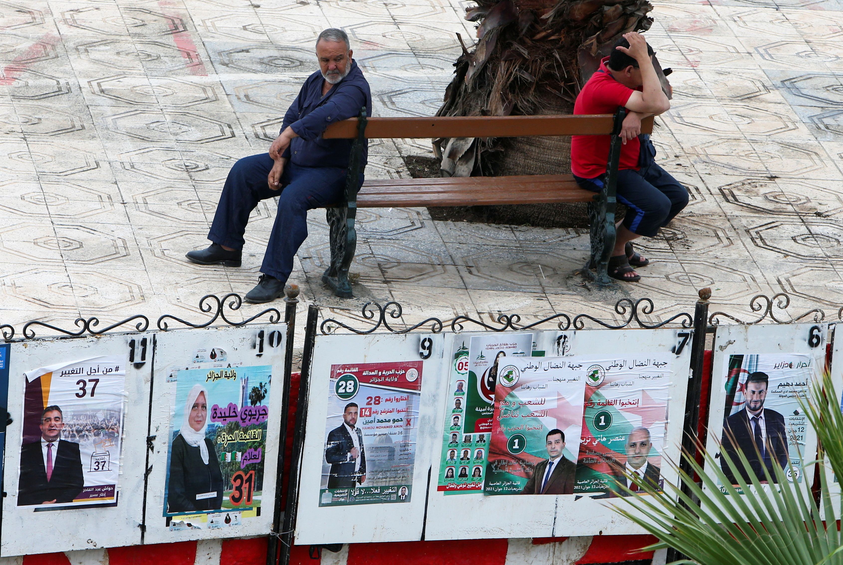 Men sit near parliamentary election campaign posters ahead of the legislative elections, in Algiers, Algeria, June 6, 2021 [File: Ramzi Boudina/Reuters]