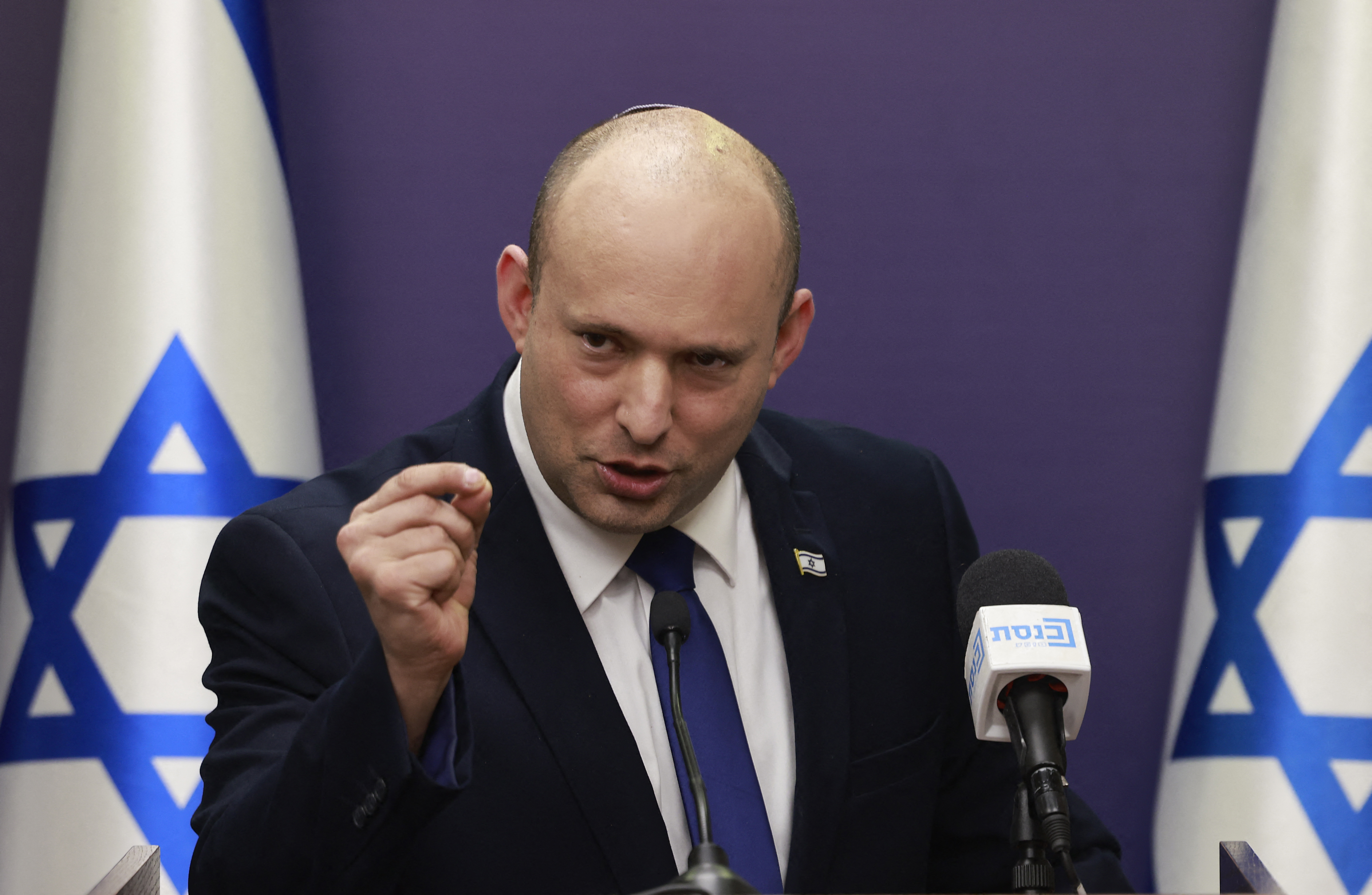 Naftali Bennett speaks at a podium in front of Israeli flags.