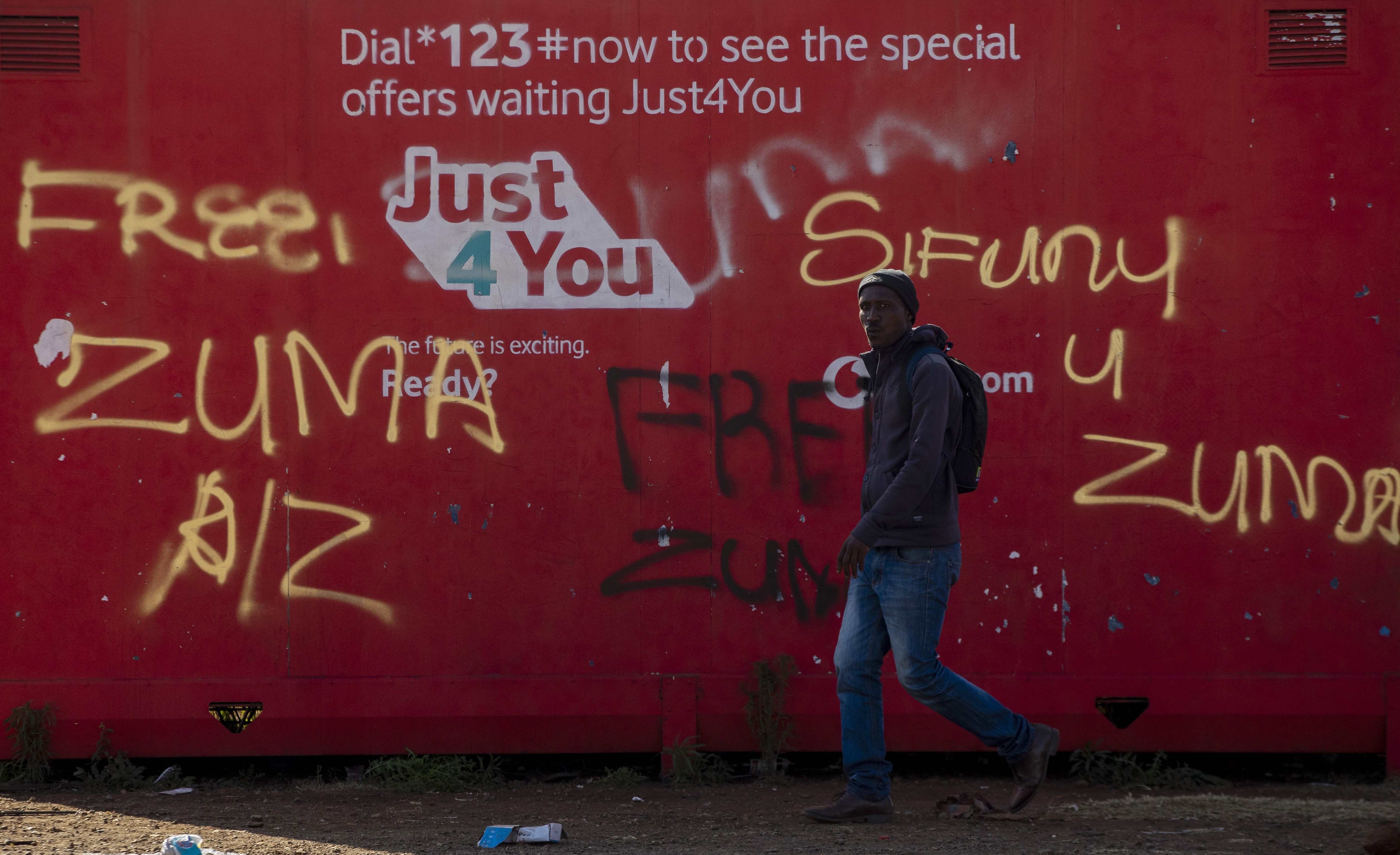 A man walks past graffiti reading "free Zuma" and "we want Zuma" outside a shopping mall in Vosloorus, east of Johannesburg, South Africa, on Wednesday, July 14, 2021 [AP Photo/Themba Hadebe]