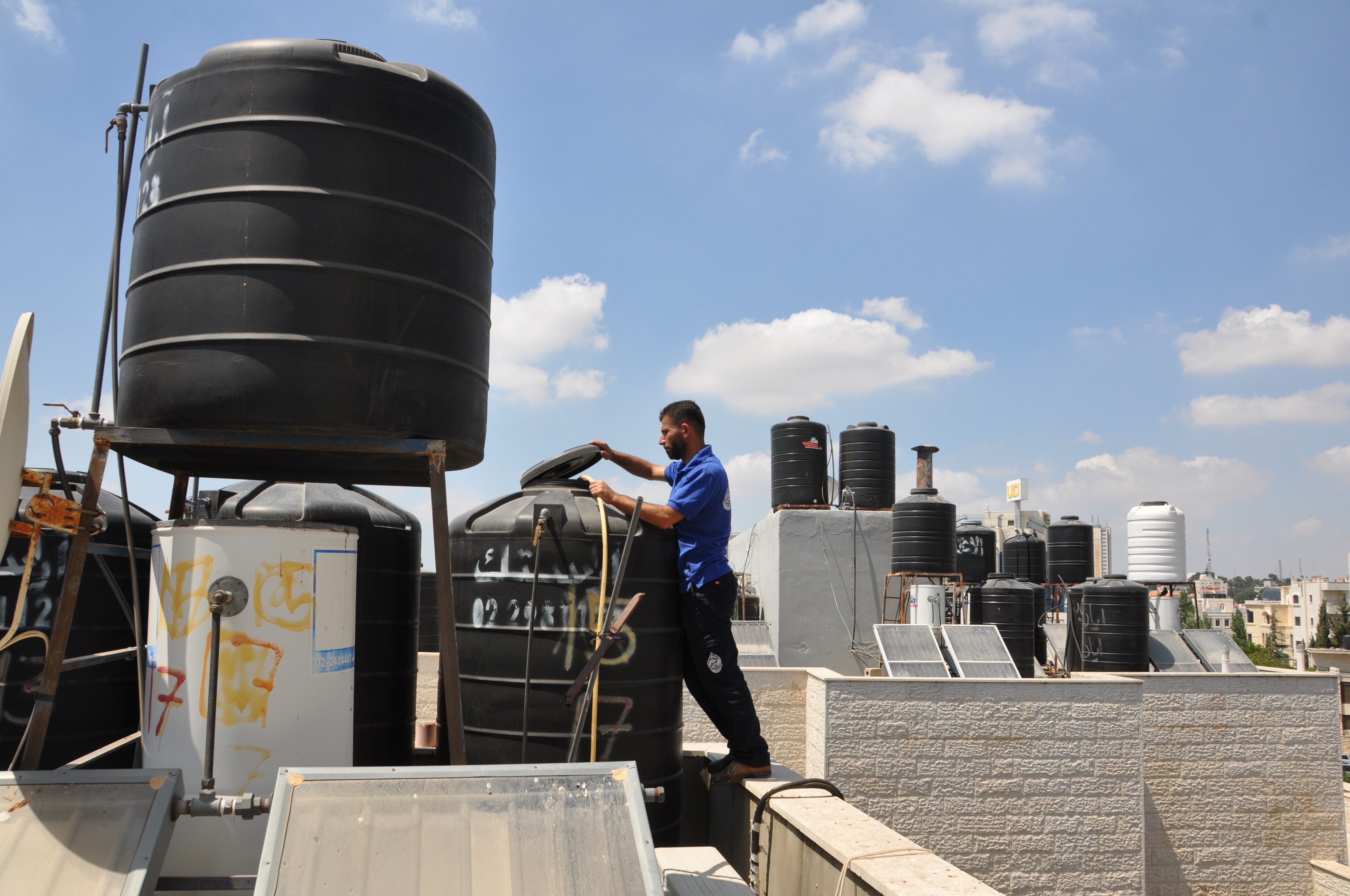 Superintendent Bassam Rayan fills residents' private water tanks at the Khawaja apartment building in Ramallah [Mohammed Najib/Al Jazeera]