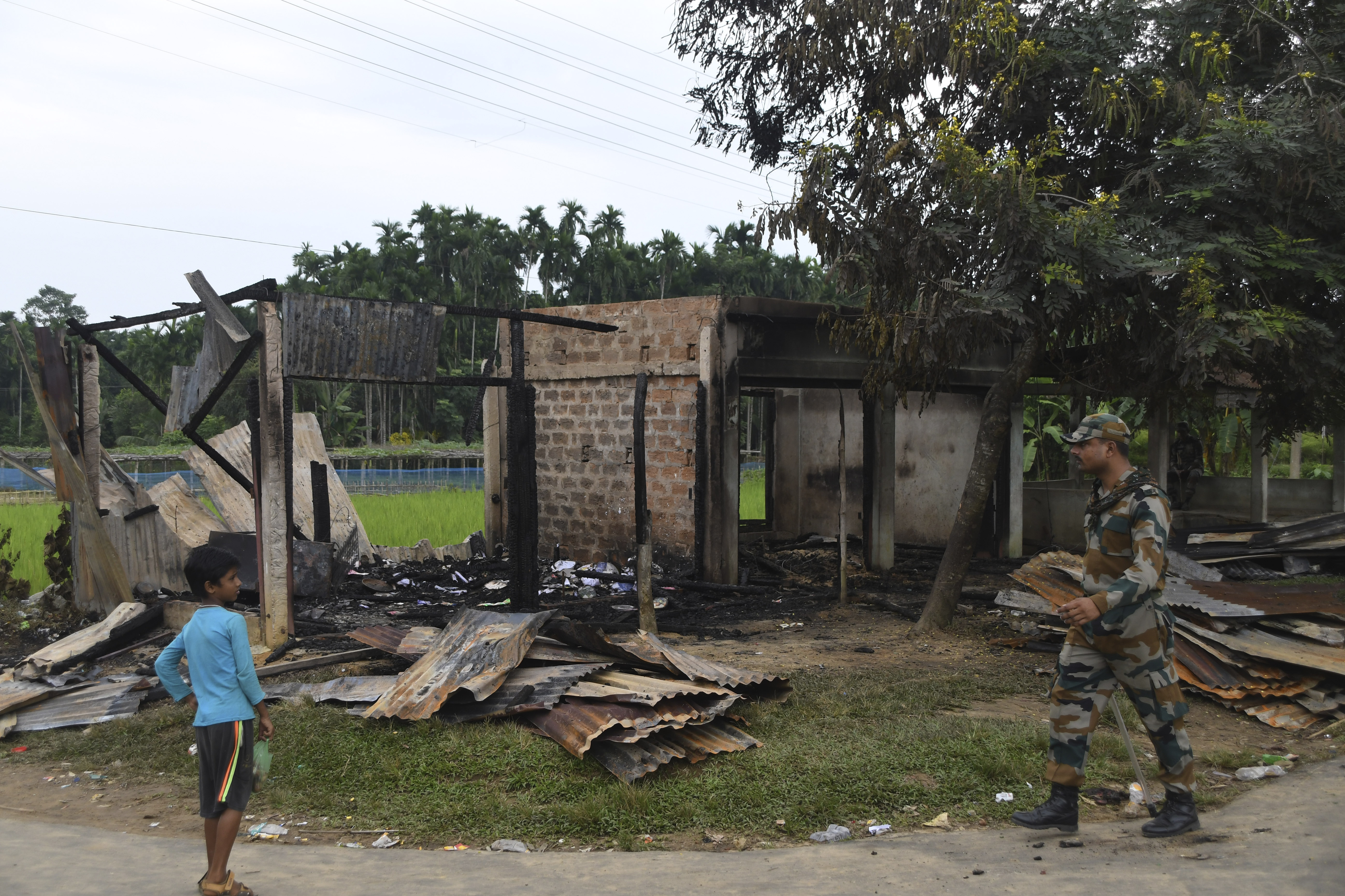 A paramilitary soldier patrols past a shop that was set on fire in Rowa village in the northeastern Indian state of Tripura [Panna Ghosh/AP]