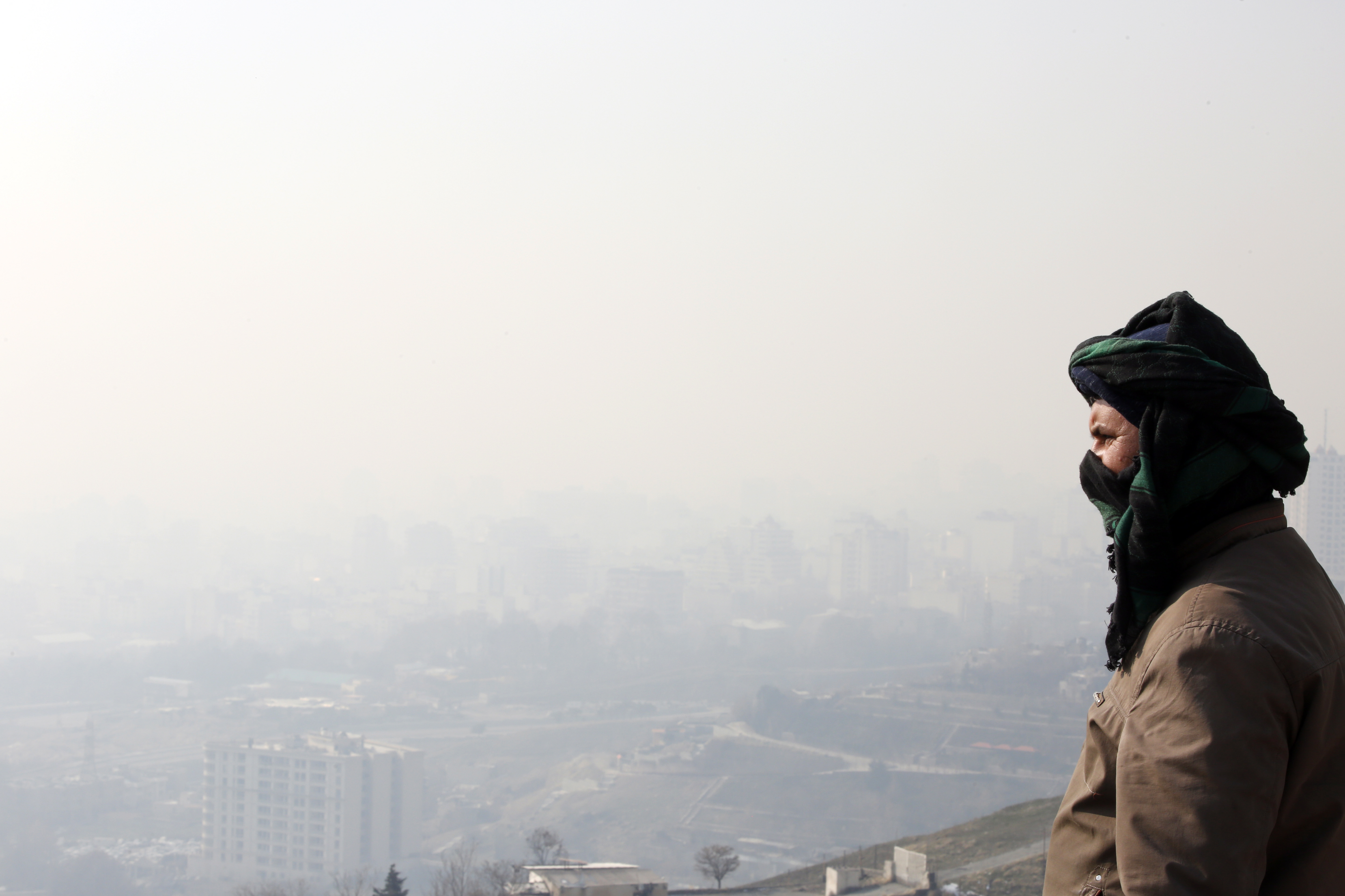 An Iranian worker looks on as smog obscures buildings in the capital Tehran [File: Abedin Taherkenareh/EPA-EFE]