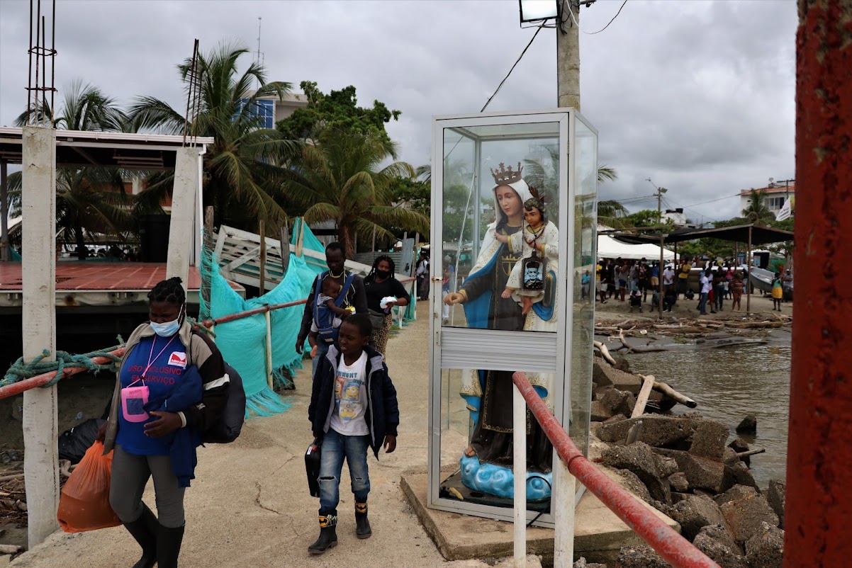 Asylum seekers and refugees pass a figure of the Virgin Mary before boarding a boat that will take them to Acandi, a town in northern Colombia on the border with Panama [Steve Grattan/Al Jazeera]