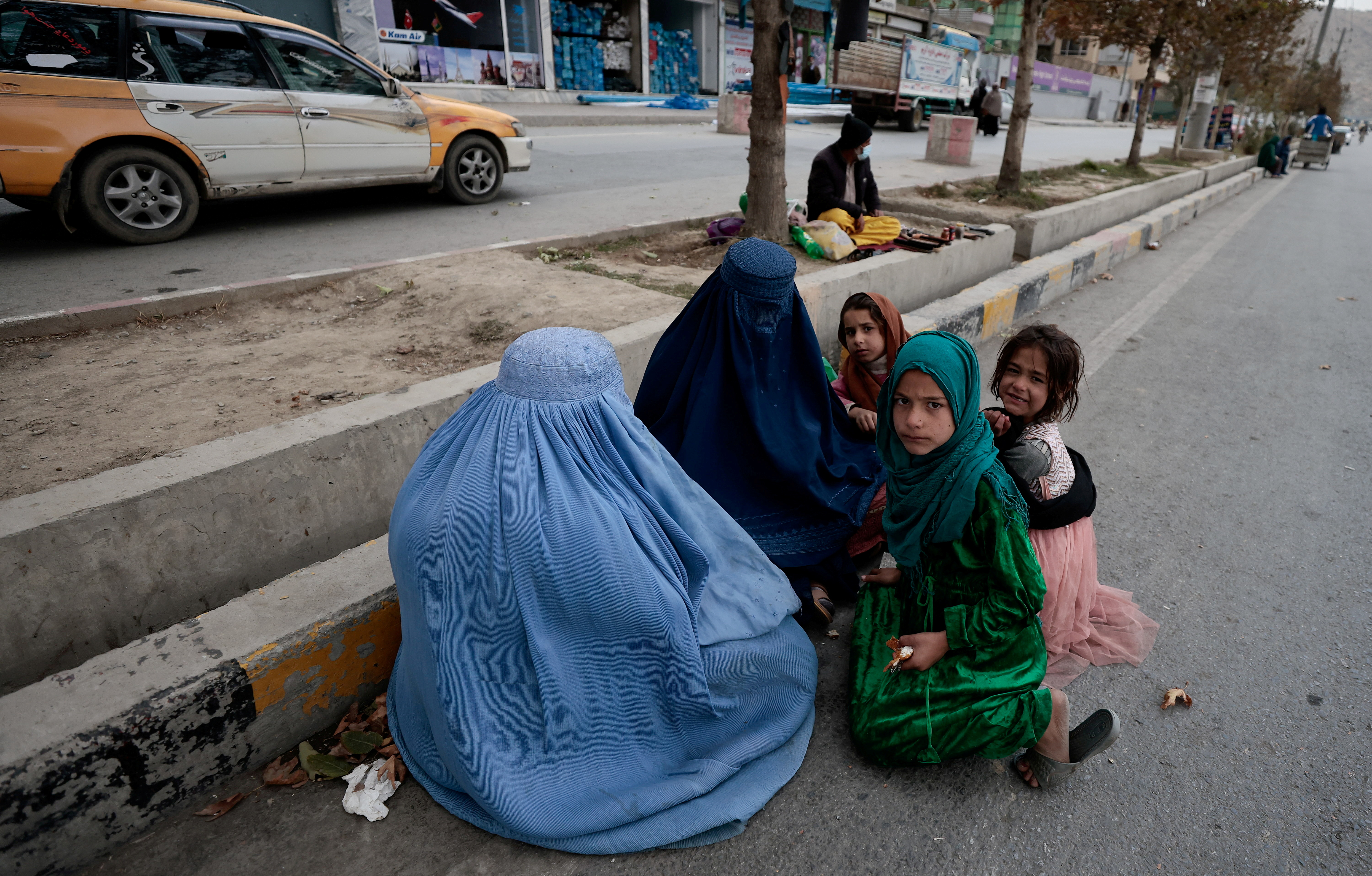 Women wearing burqas sit with their children as they beg along a road in Kabul on October 26, 2021 [Reuters/Zohra Bensemra]