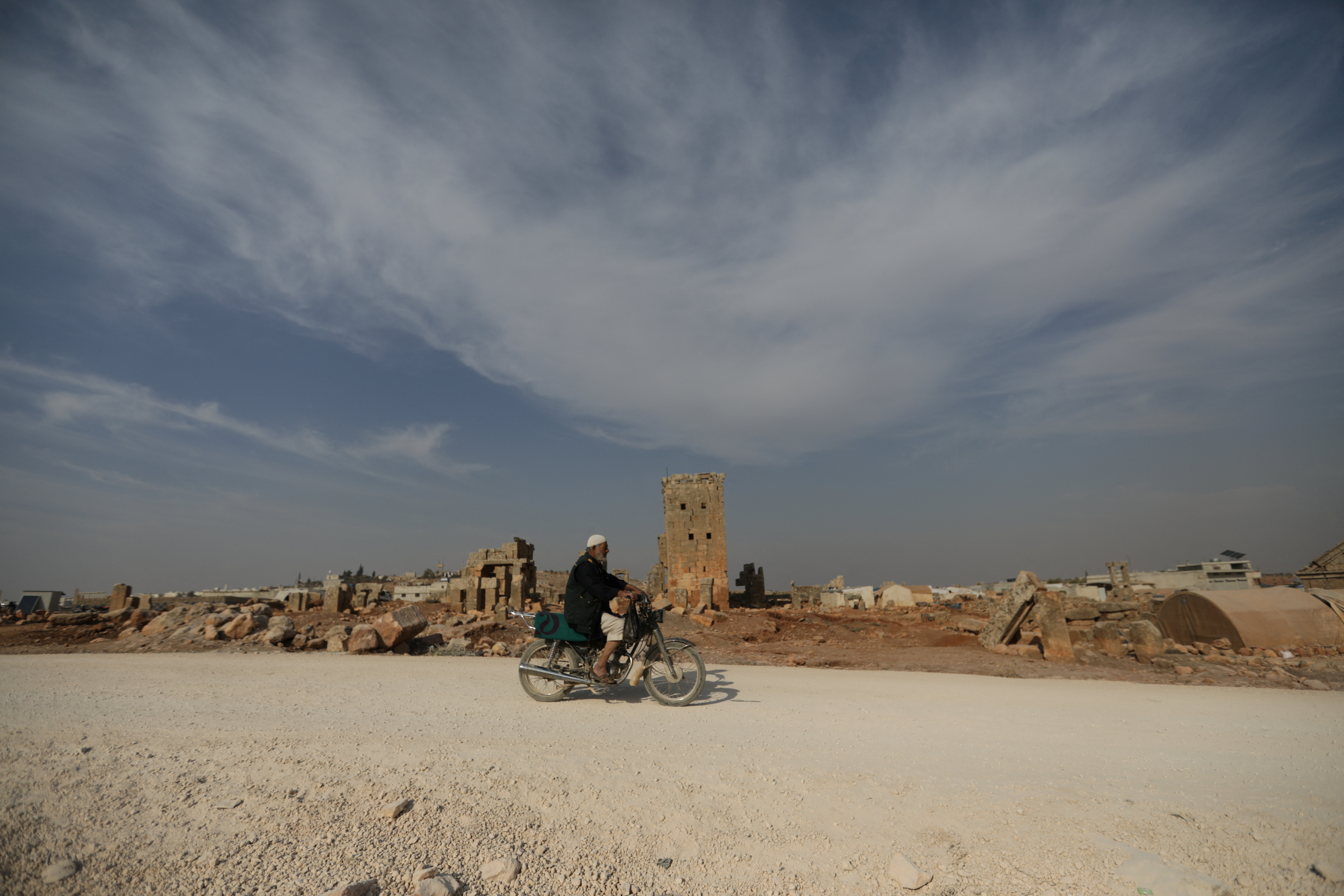 A man rides a motorcycle through the archaeological site of Sarjableh, Syria
