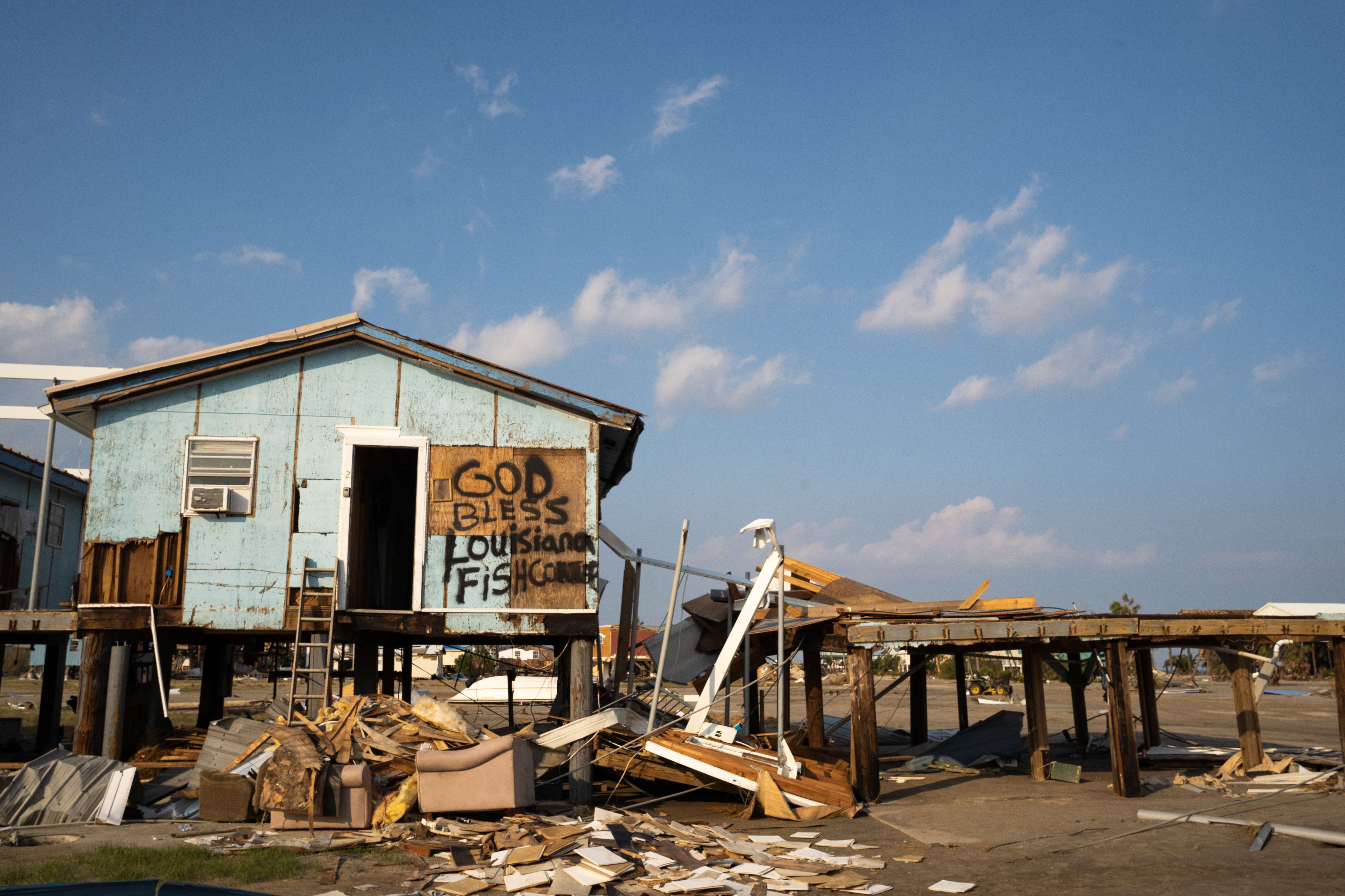 A photo of a wrecked house with bits and pieces of wood and scrap in front of it.