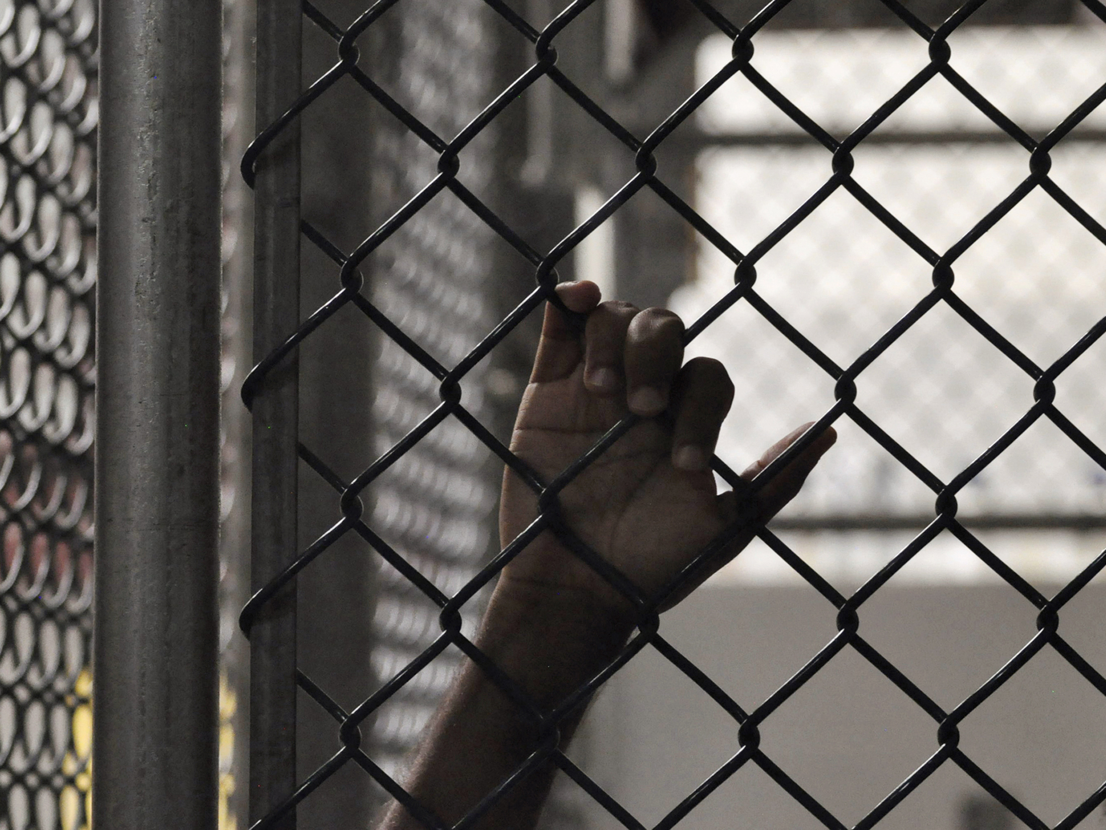 The hand of a Guantanamo detainee is seen holding onto a fence