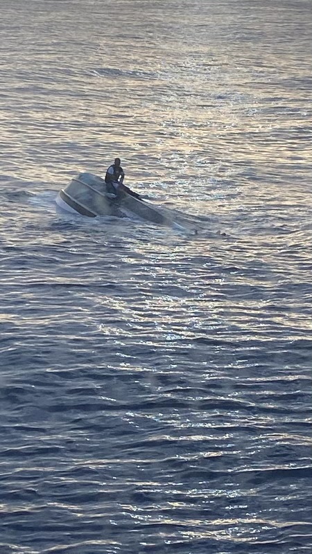 A man clings onto the hull of a capsized boat in the sea between Florida and Miami